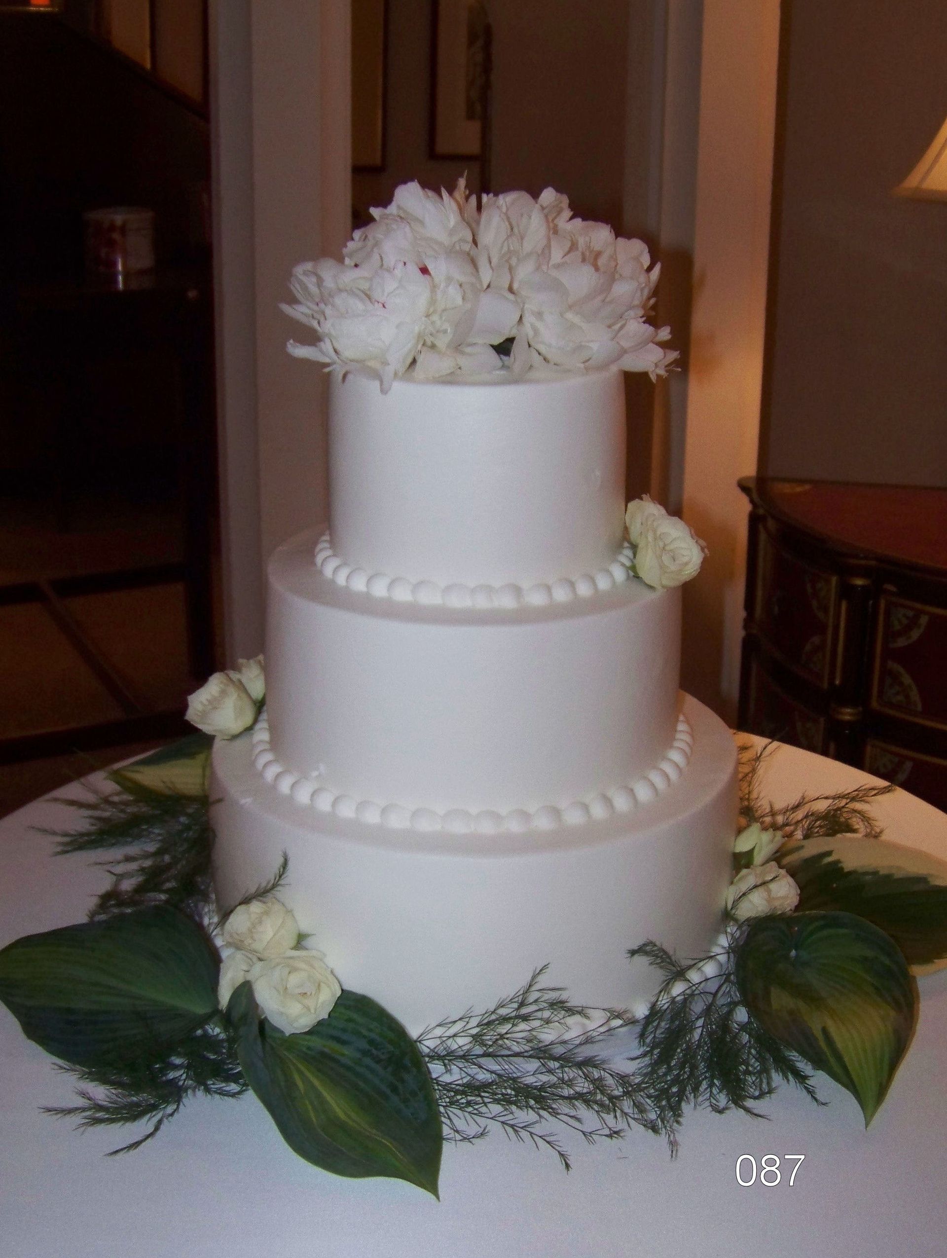 Three-tier white wedding cake with white flowers and green leaves on a table