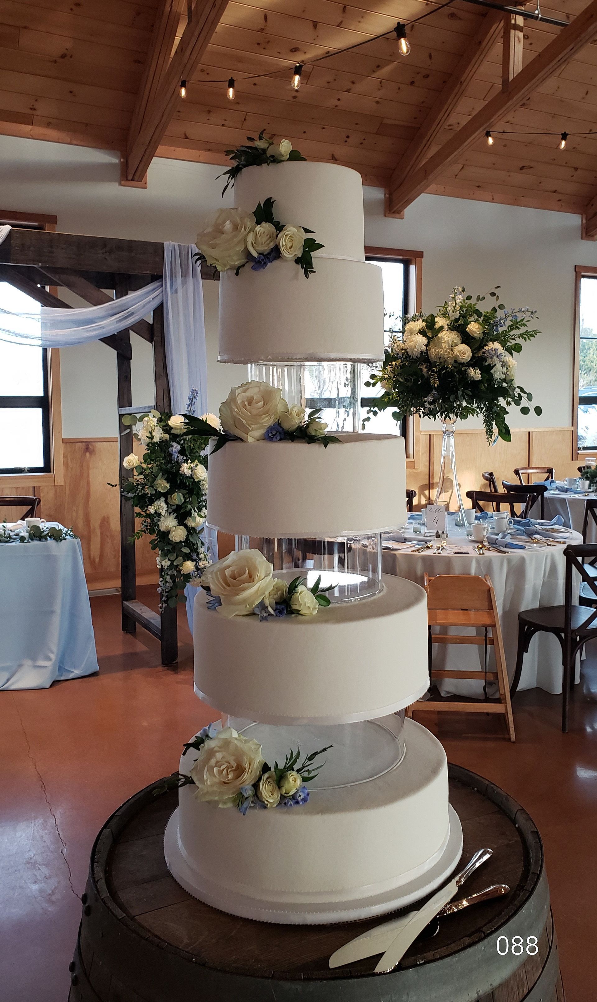 Four-tier white wedding cake decorated with pastel flowers on a base in a reception hall