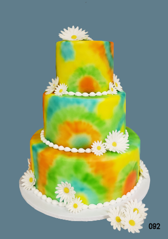 Three-tier cake with yellow and green tie-dye frosting and white daisy flowers on a white stand