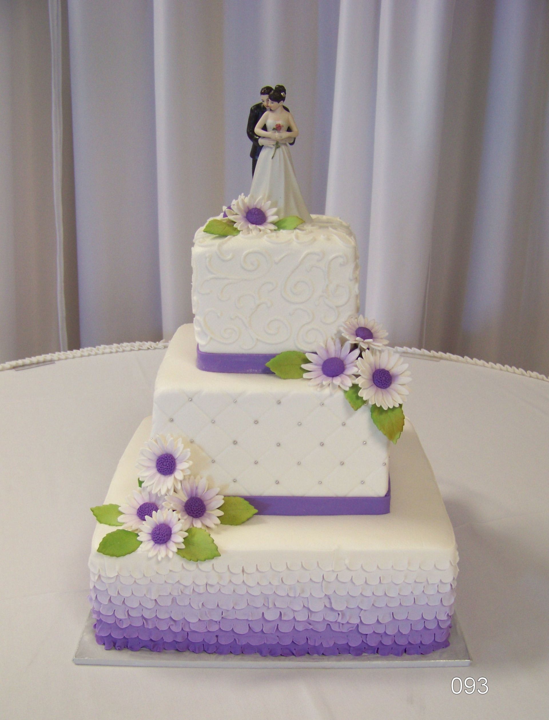 Three-tier white cake with purple accents and flowers, topped with a small bride figurine