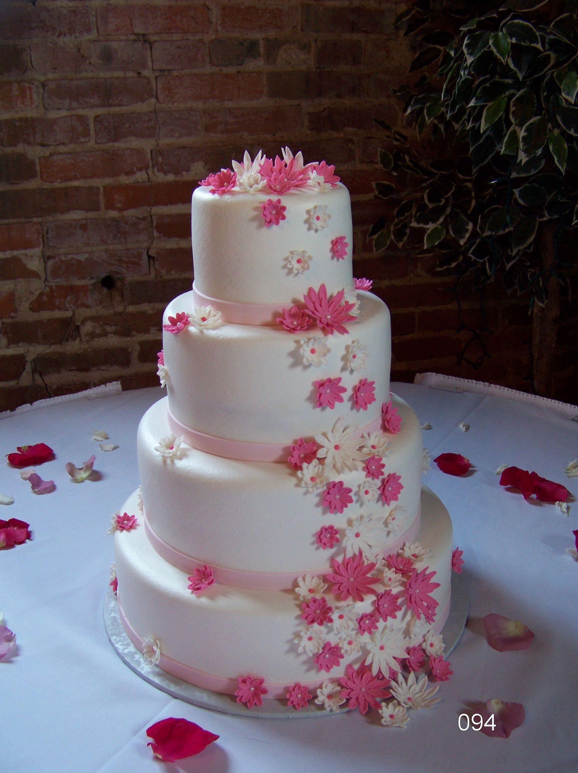 Four-tier white wedding cake with pink flowers on a round table