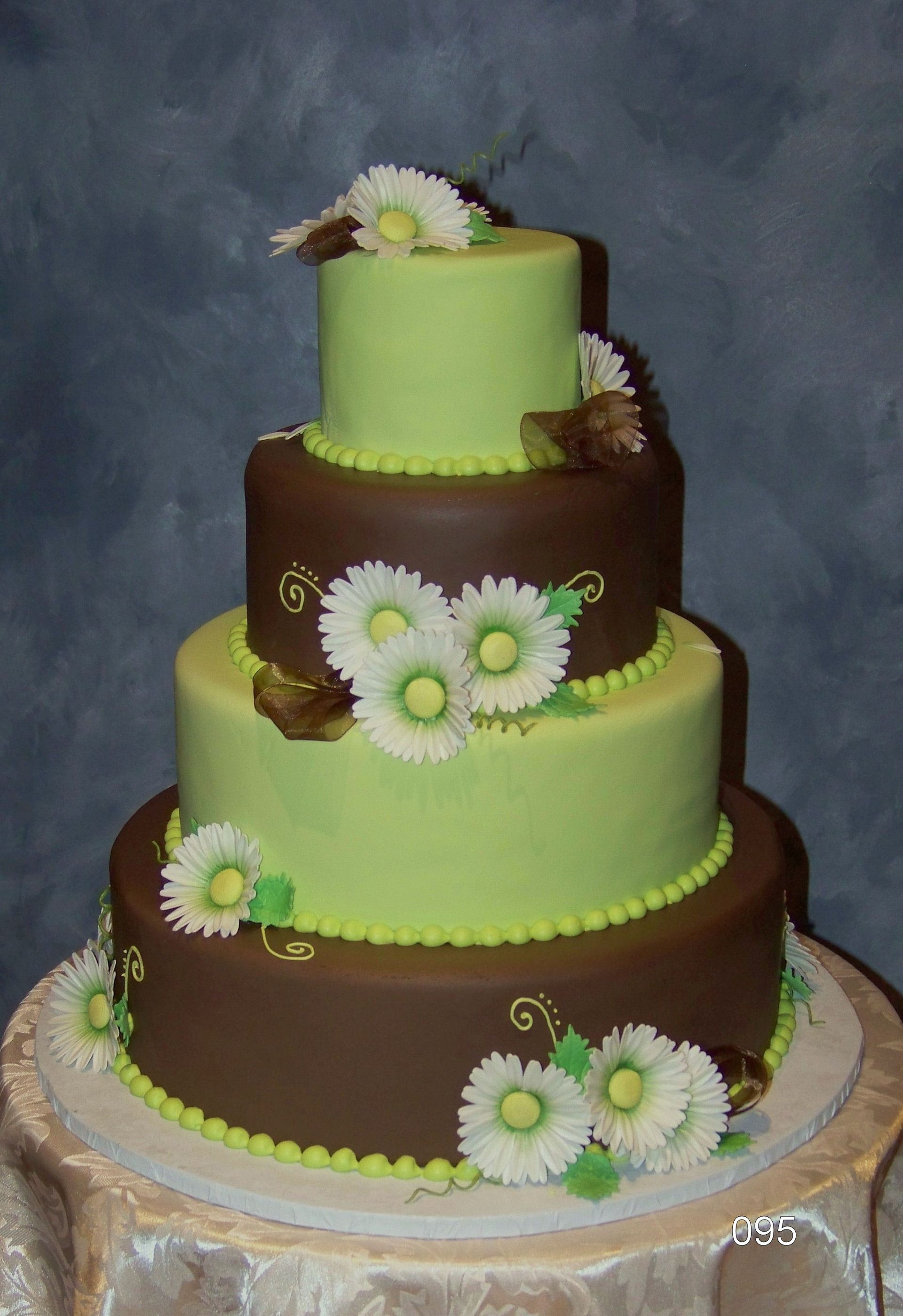 Four-tier cake with lime-green and chocolate layers, decorated with white daisies on a silver board