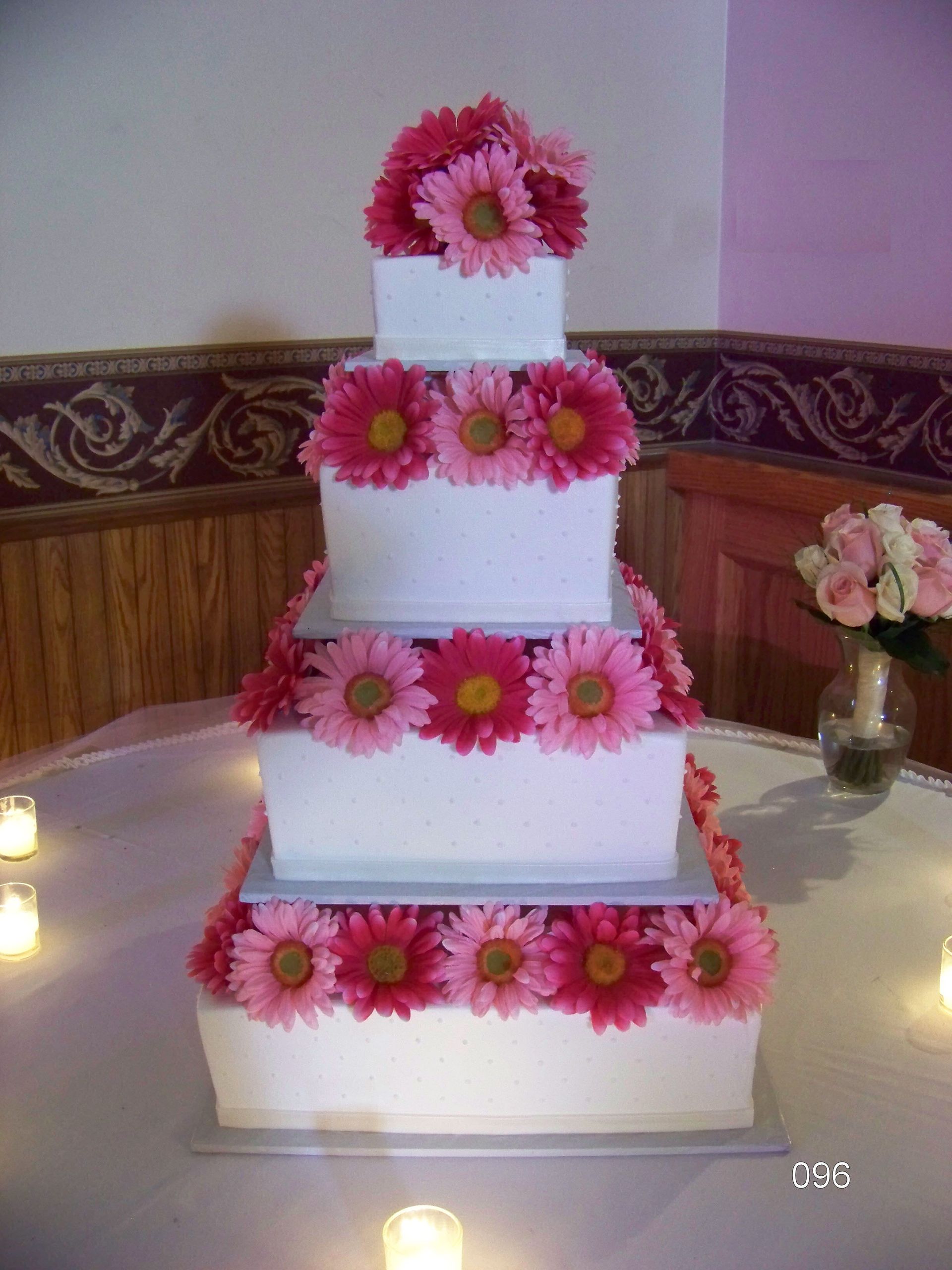 Tiered white cake decorated with pink flowers at a candlelit party table.