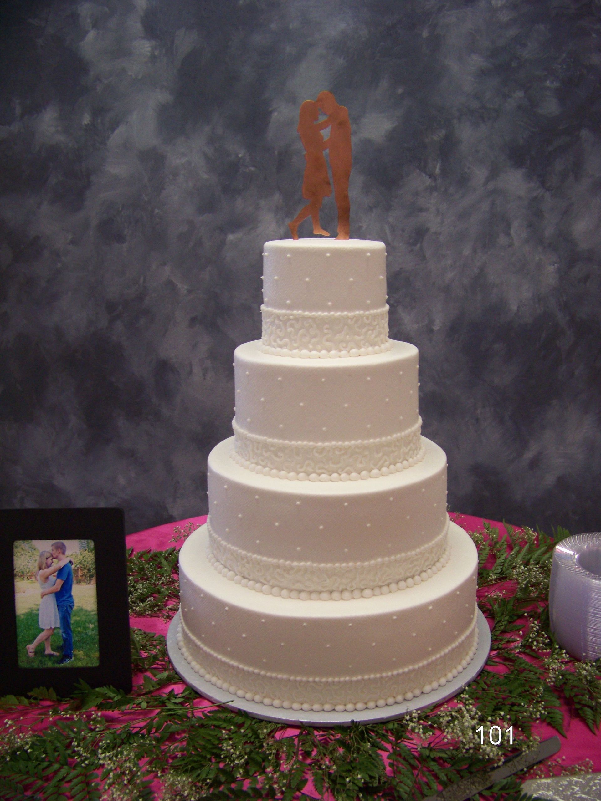 Four-tier white wedding cake with a couple topper and floral decorations on a table