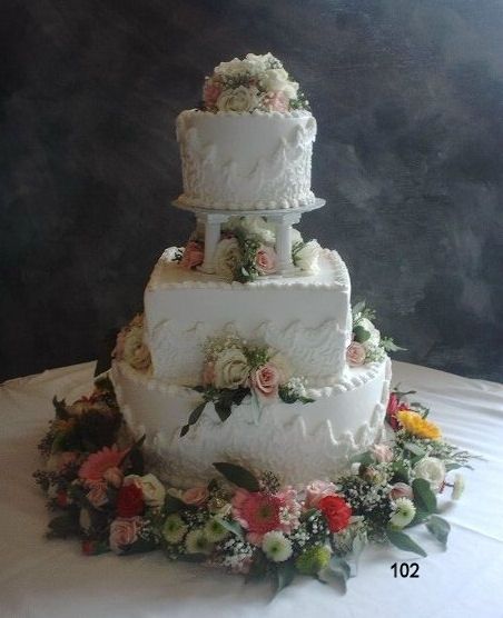 Three-tier white wedding cake with pink flowers and greenery on a table