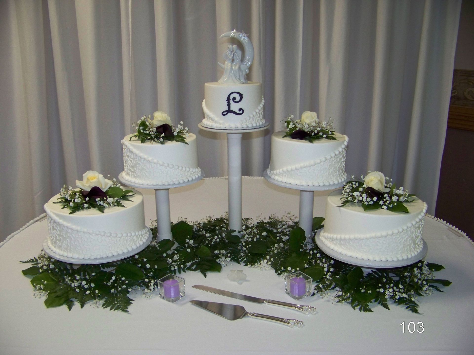 White tiered wedding cake display with silver accents, floral decorations, and the letter “L” on top