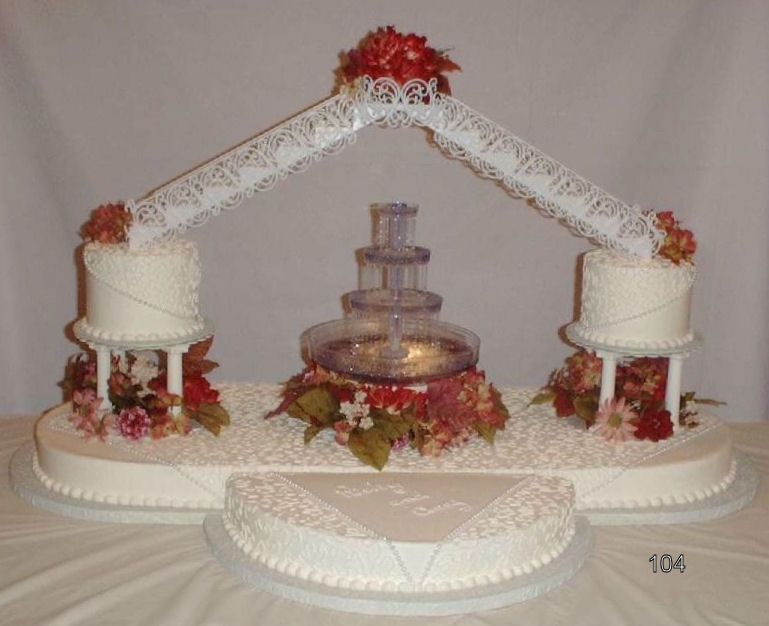 White wedding cake with lace arch, floral decorations, and a central fountain on a table