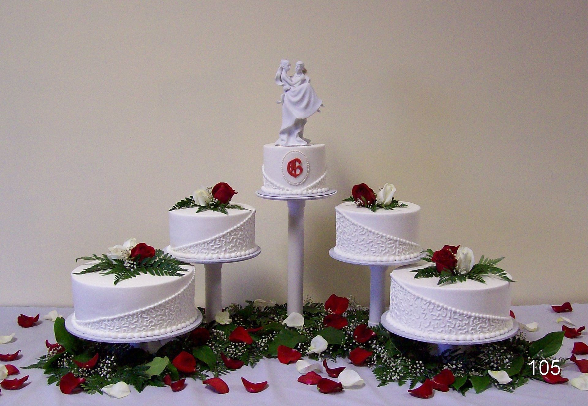 White tiered cake display with red rose decorations and a figurine topper on a table