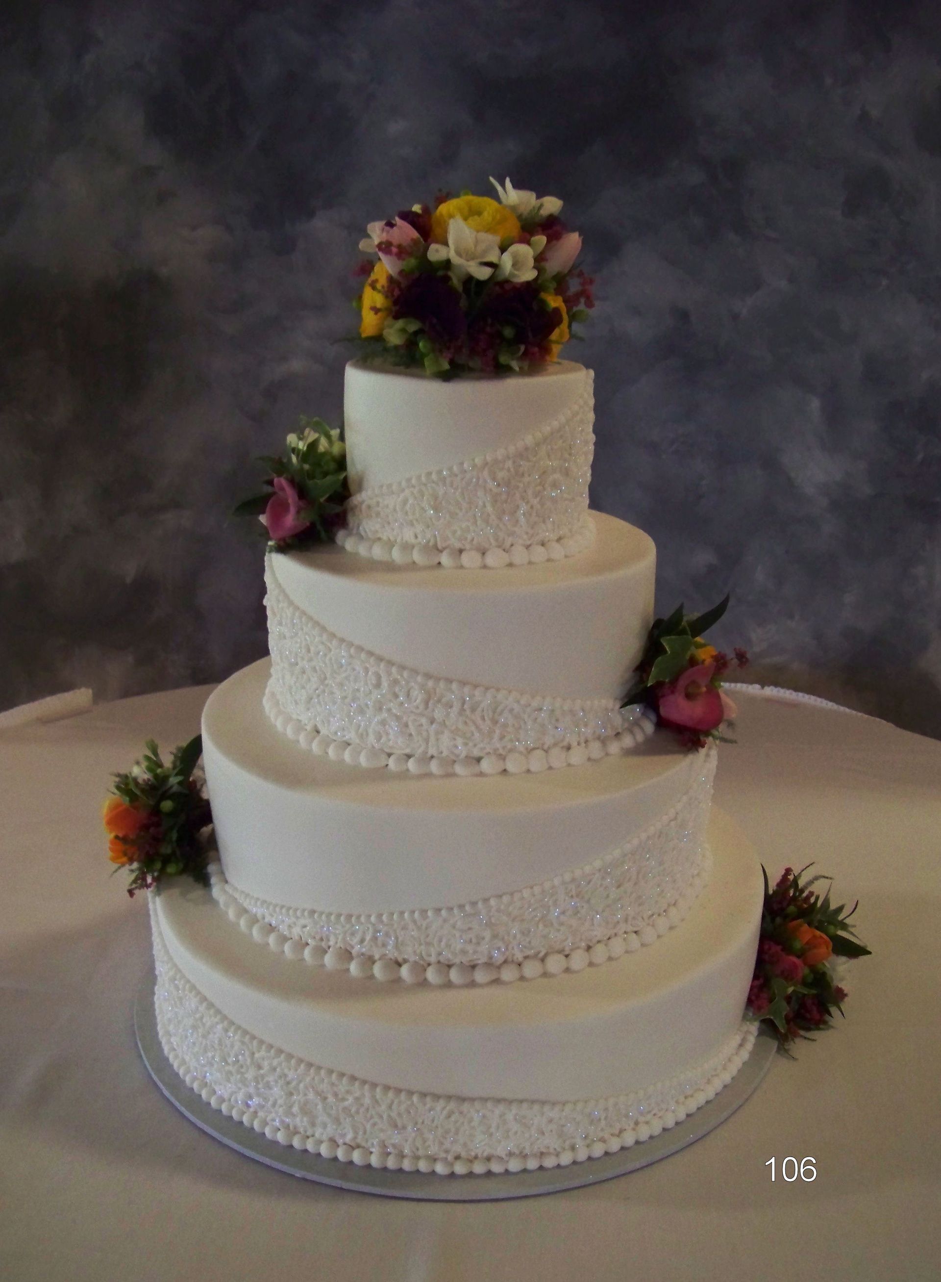 Four-tier white wedding cake with floral decorations on a table against a dark backdrop