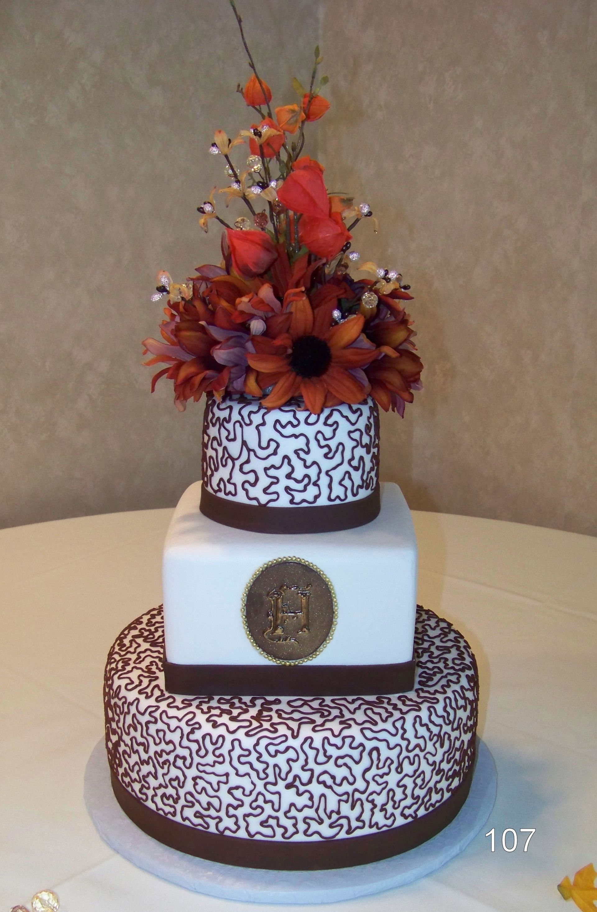 Three-tier white cake with brown swirl pattern and orange-red floral topper on a table
