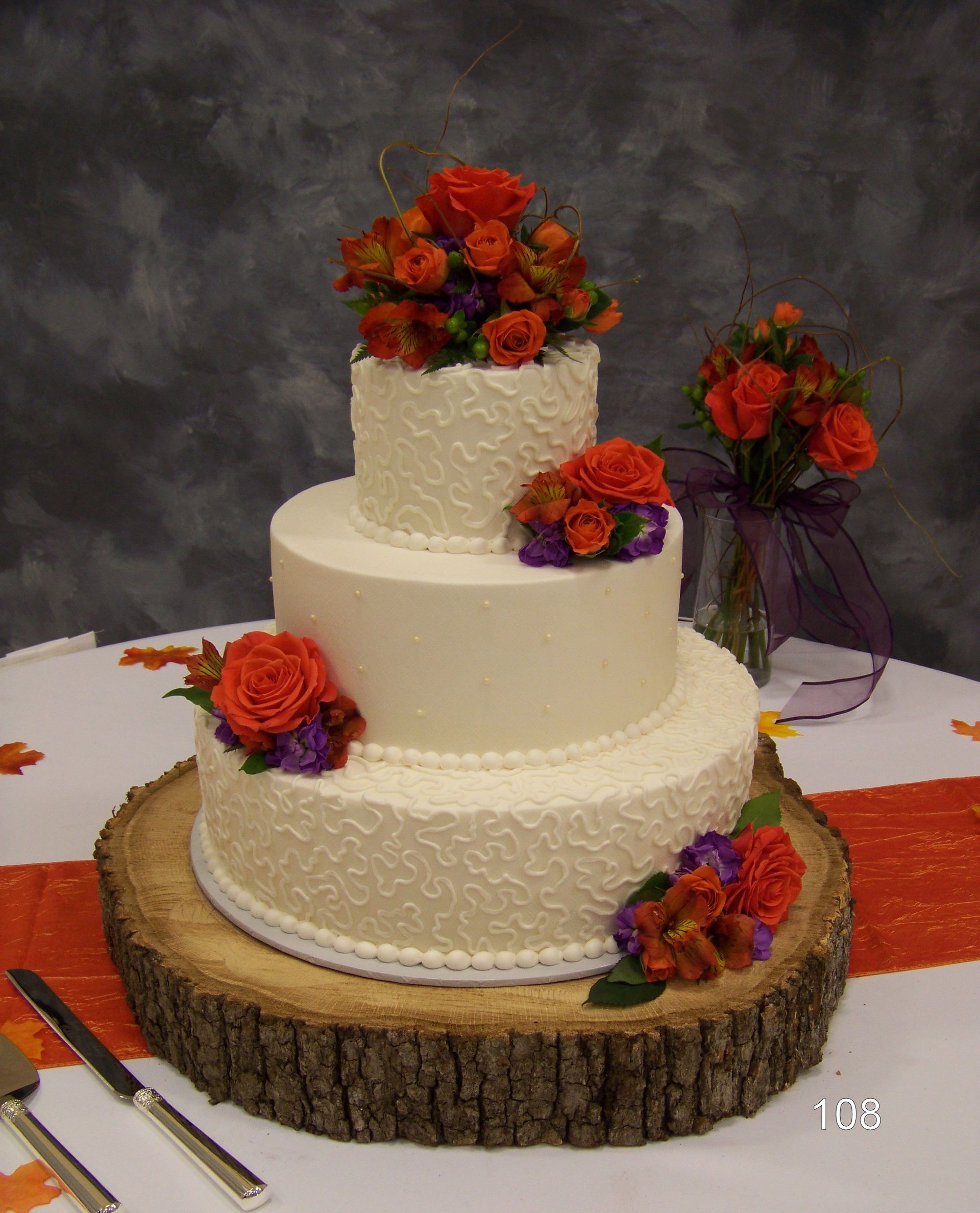 Three-tier white wedding cake with orange and purple flowers on a rustic wood slab