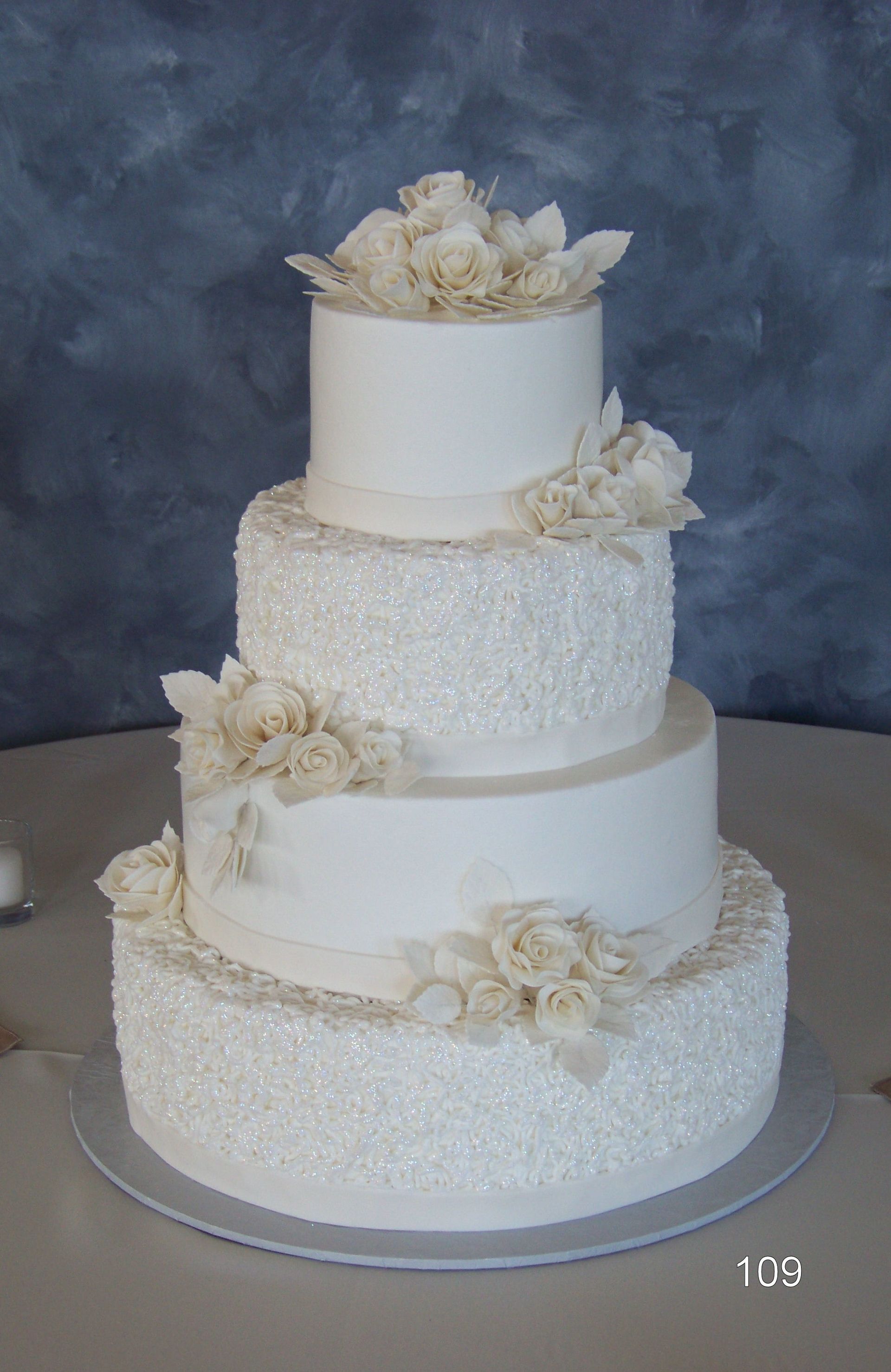 Four-tier white wedding cake with ivory floral decorations on a gray backdrop