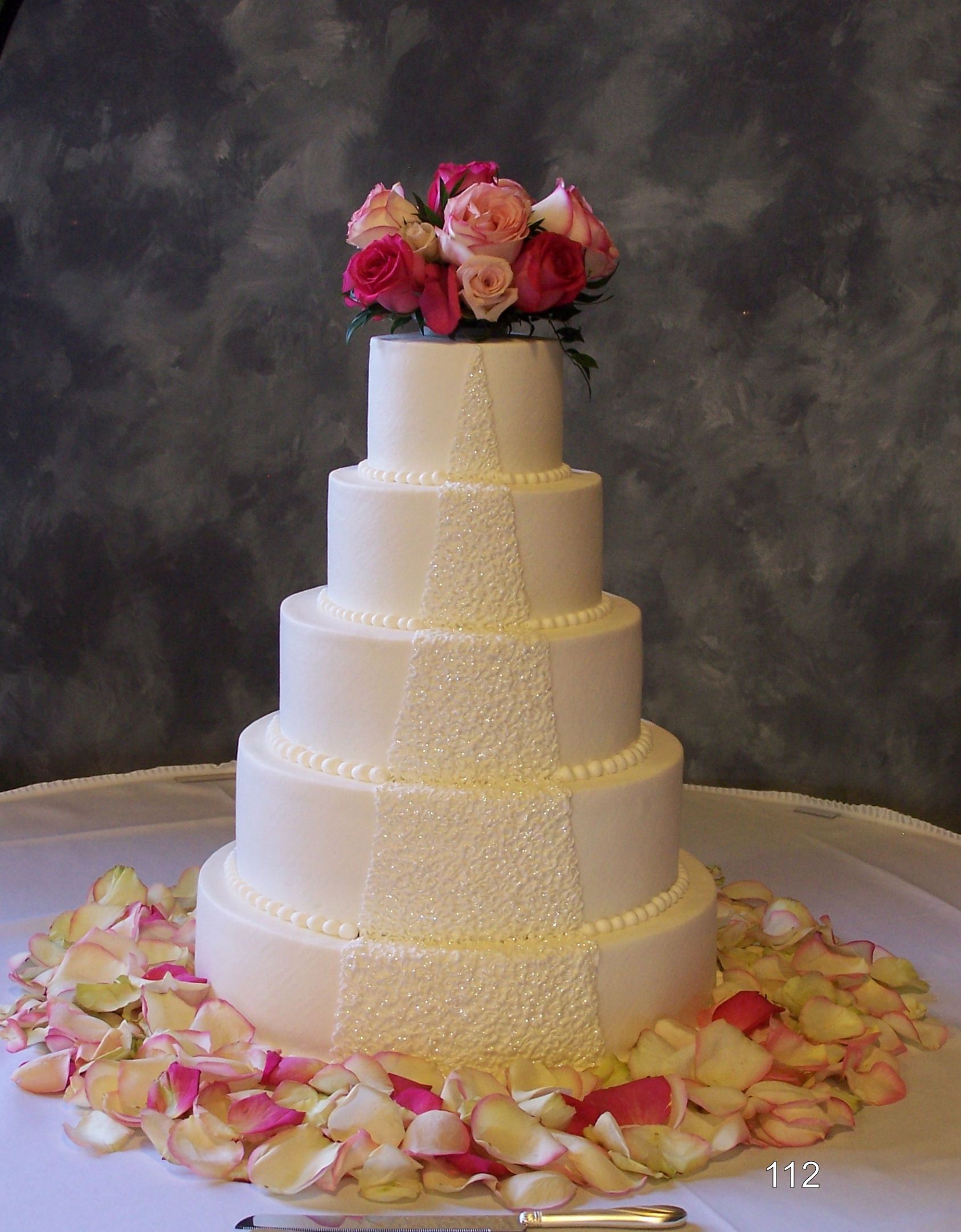 Five-tier white wedding cake with pink flowers and rose petals on a table