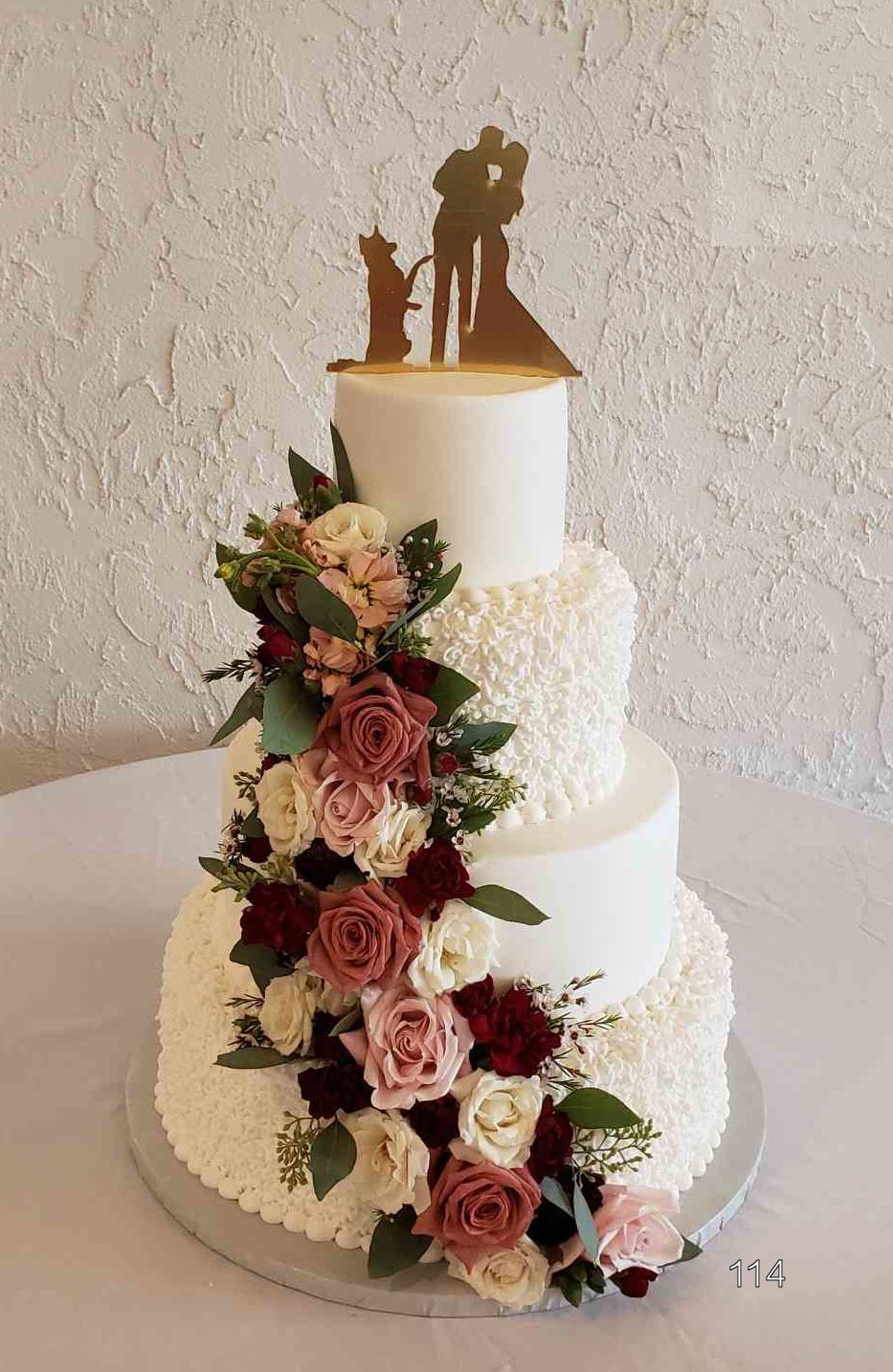 Three-tier white wedding cake with cascading pink roses and gold bride-and-groom topper
