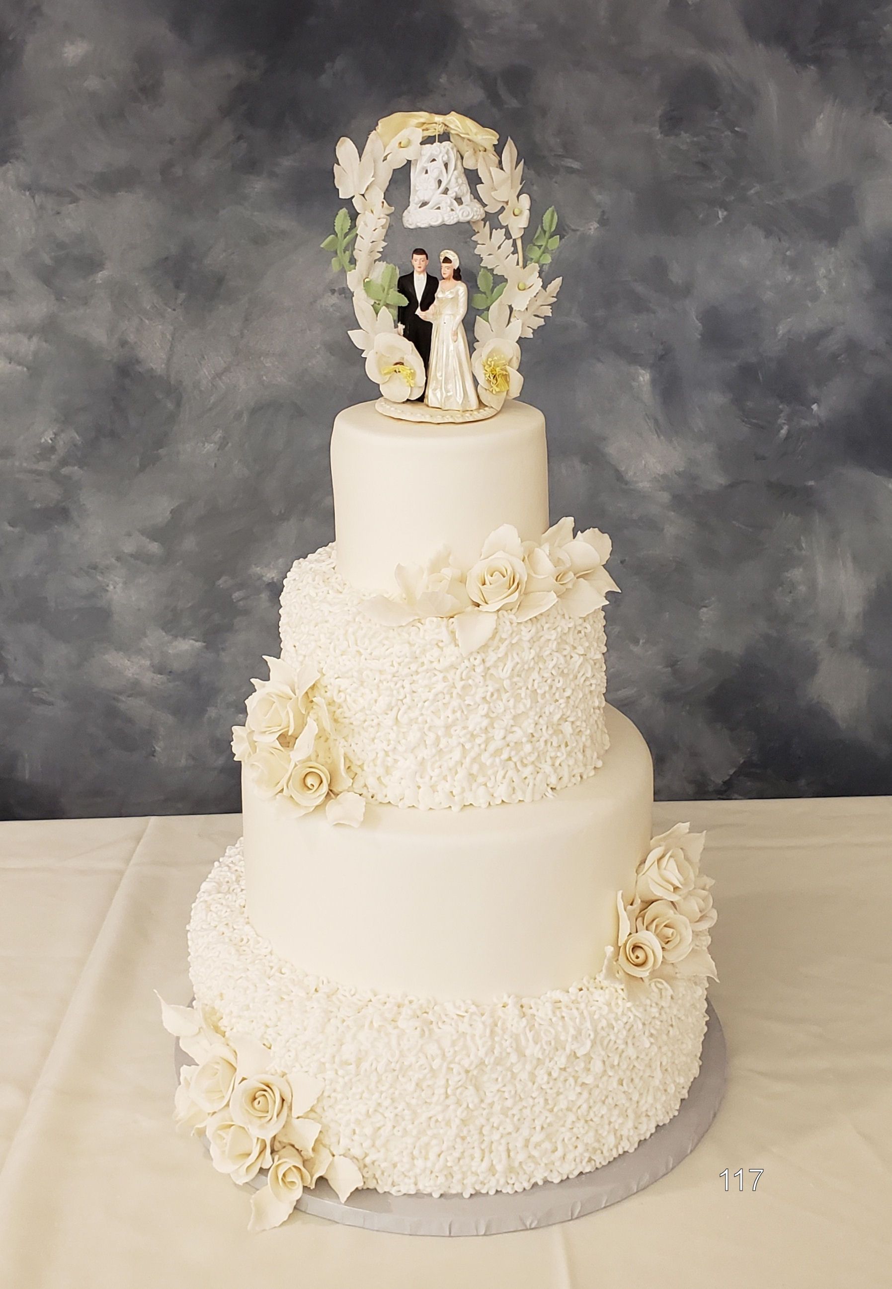Three-tier white wedding cake with cream flowers and a bride-and-groom topper