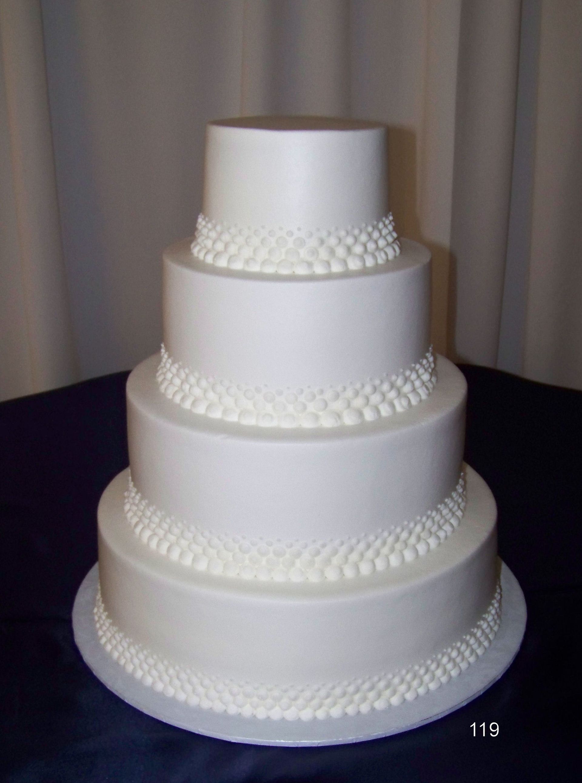 Four-tier white wedding cake with decorative pearl-like trim on each layer