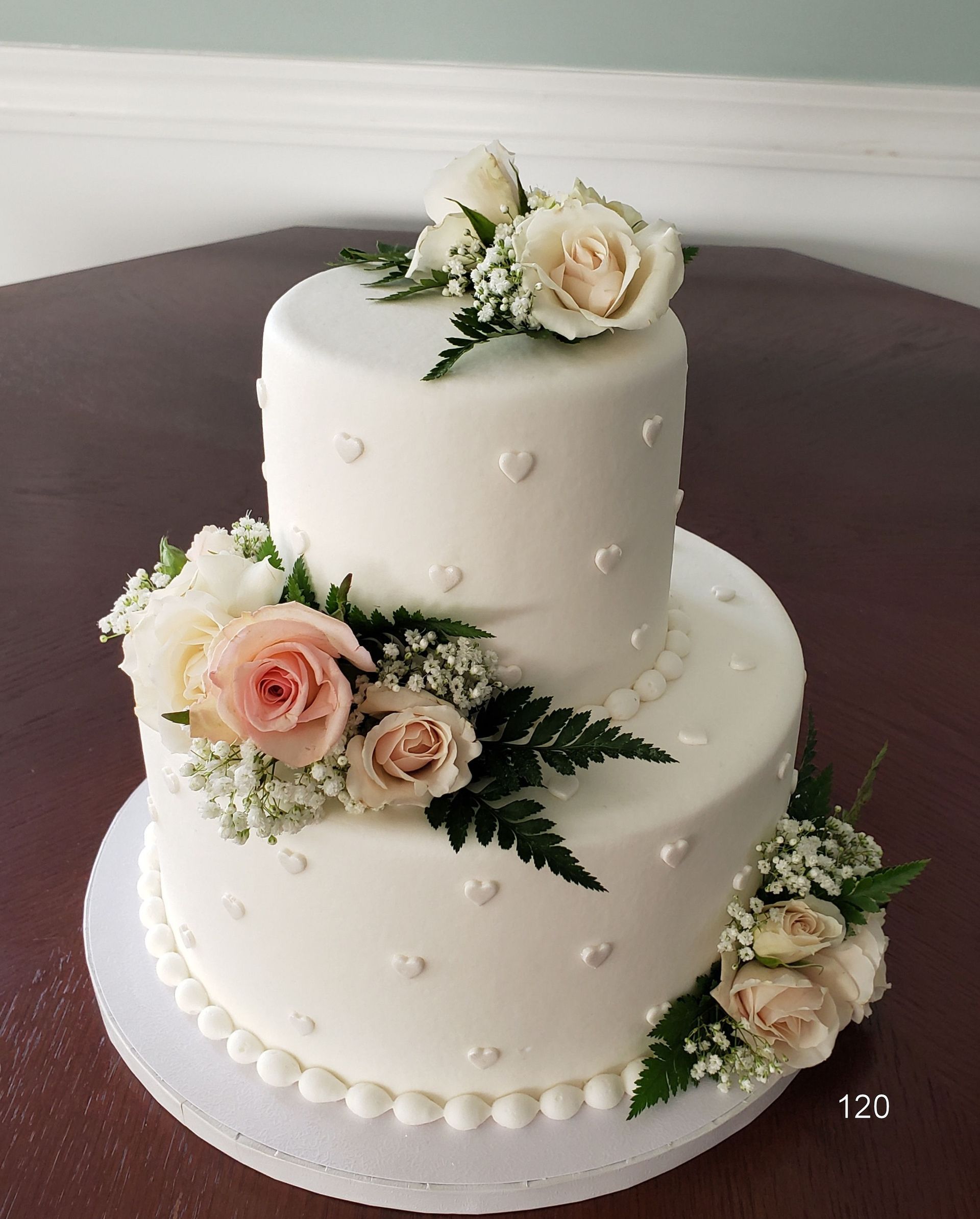 White two-tier wedding cake with pearl dots and blush roses on a dark table