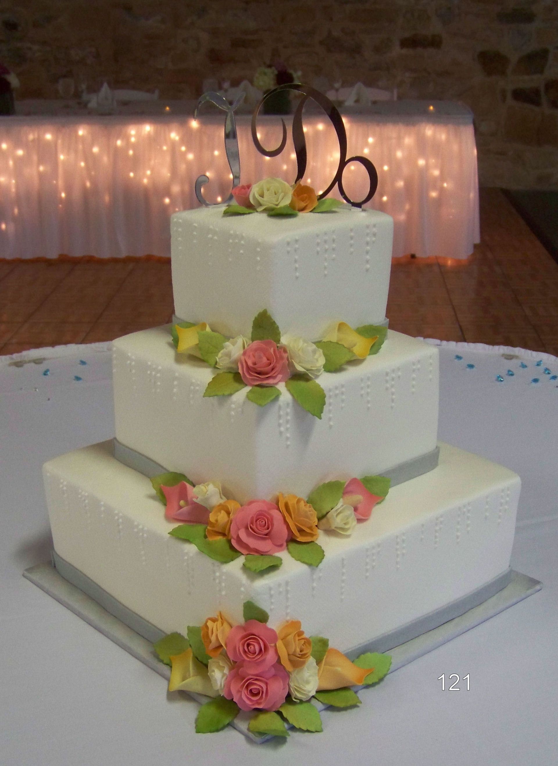 Three-tier white wedding cake with pink and peach flowers on a white table