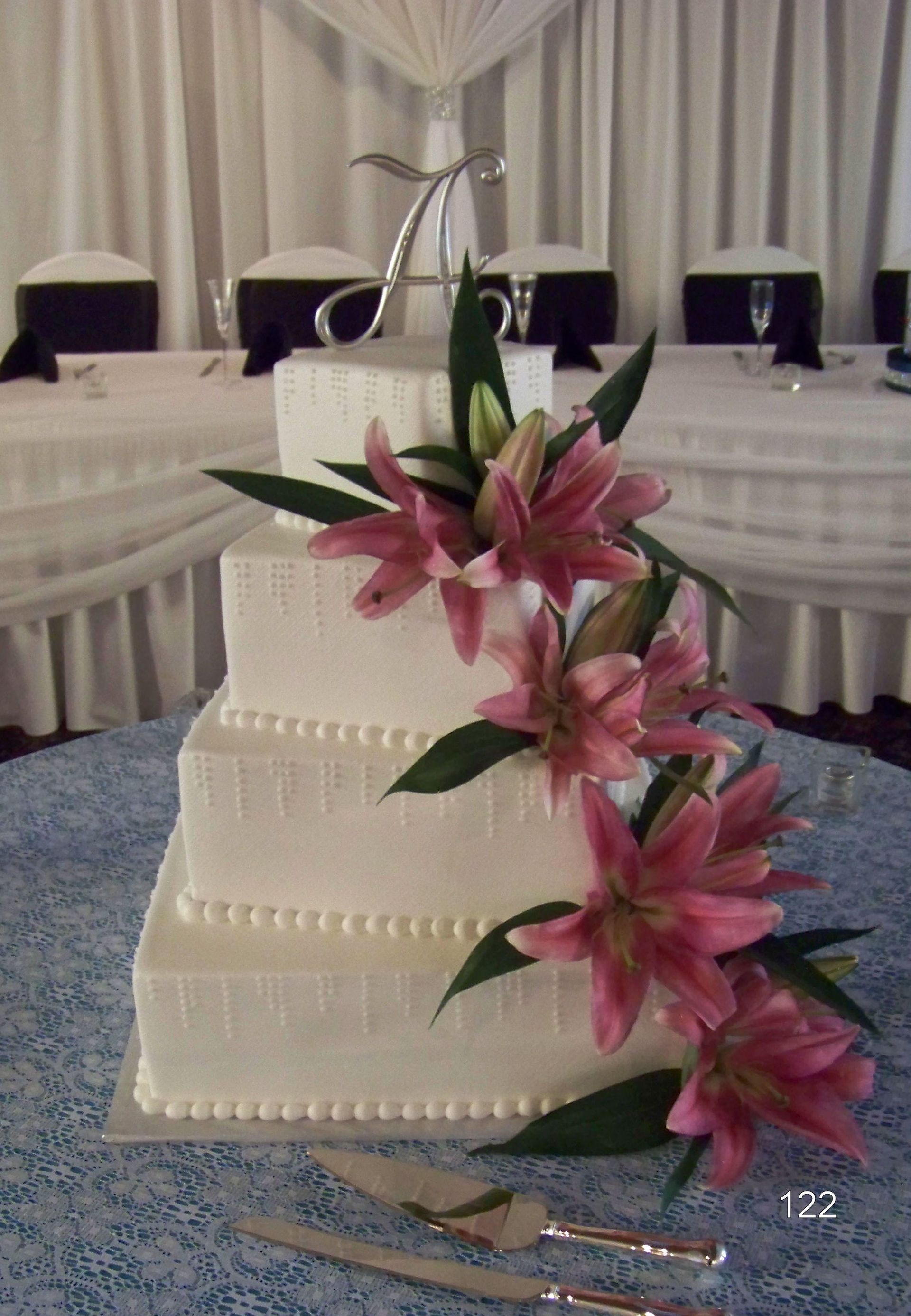 Three-tier white wedding cake with pink lilies on a banquet table in a decorated room