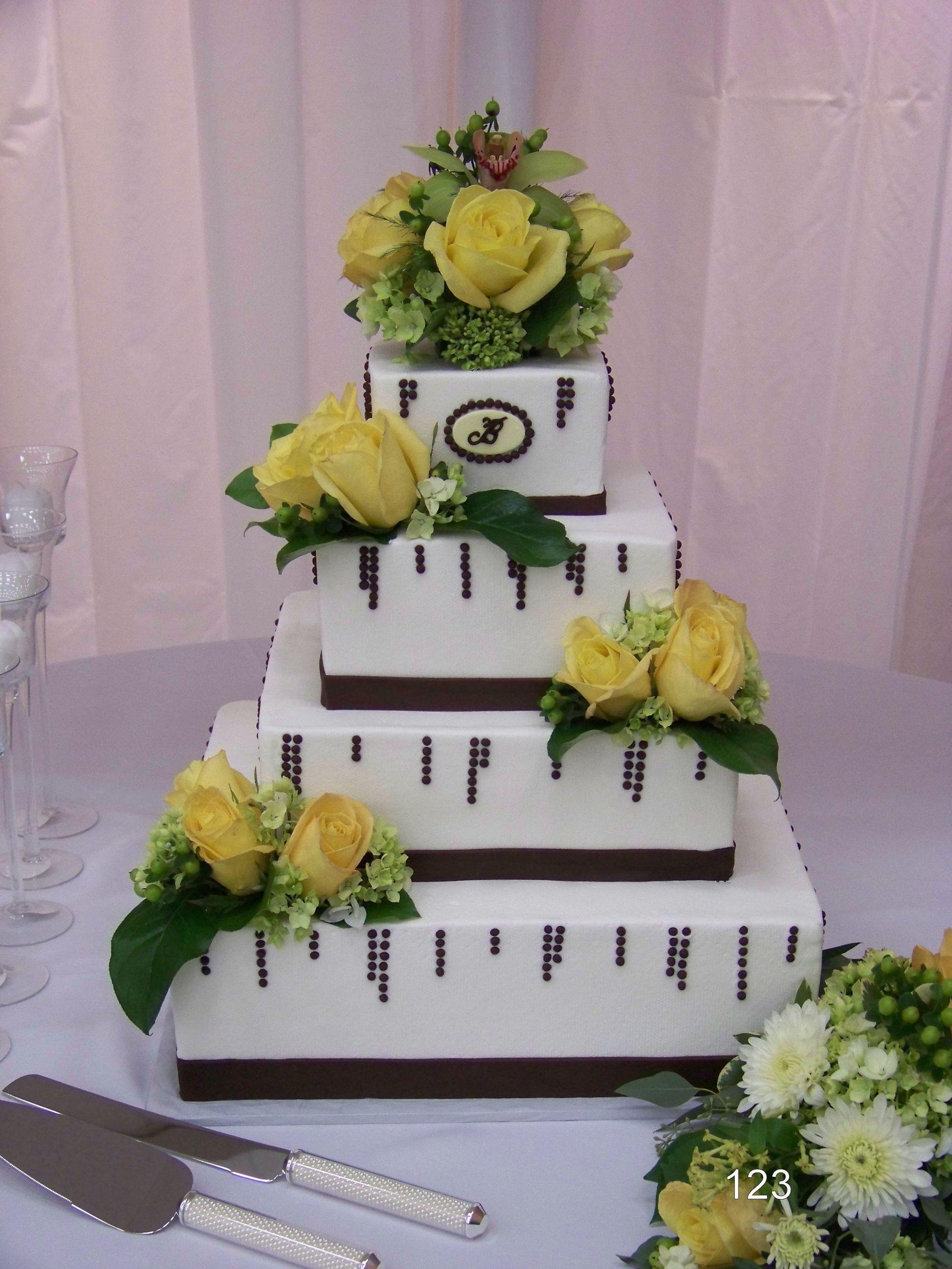 Tiered white wedding cake with yellow roses and green leaves on a table
