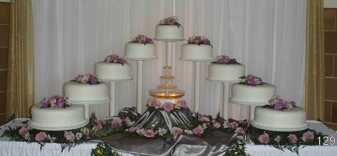 Tiered white wedding cake with pink flowers and draped ivory frosting on a decorated table