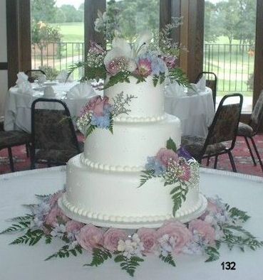 Three-tier white wedding cake with pink and purple floral decorations on a reception table