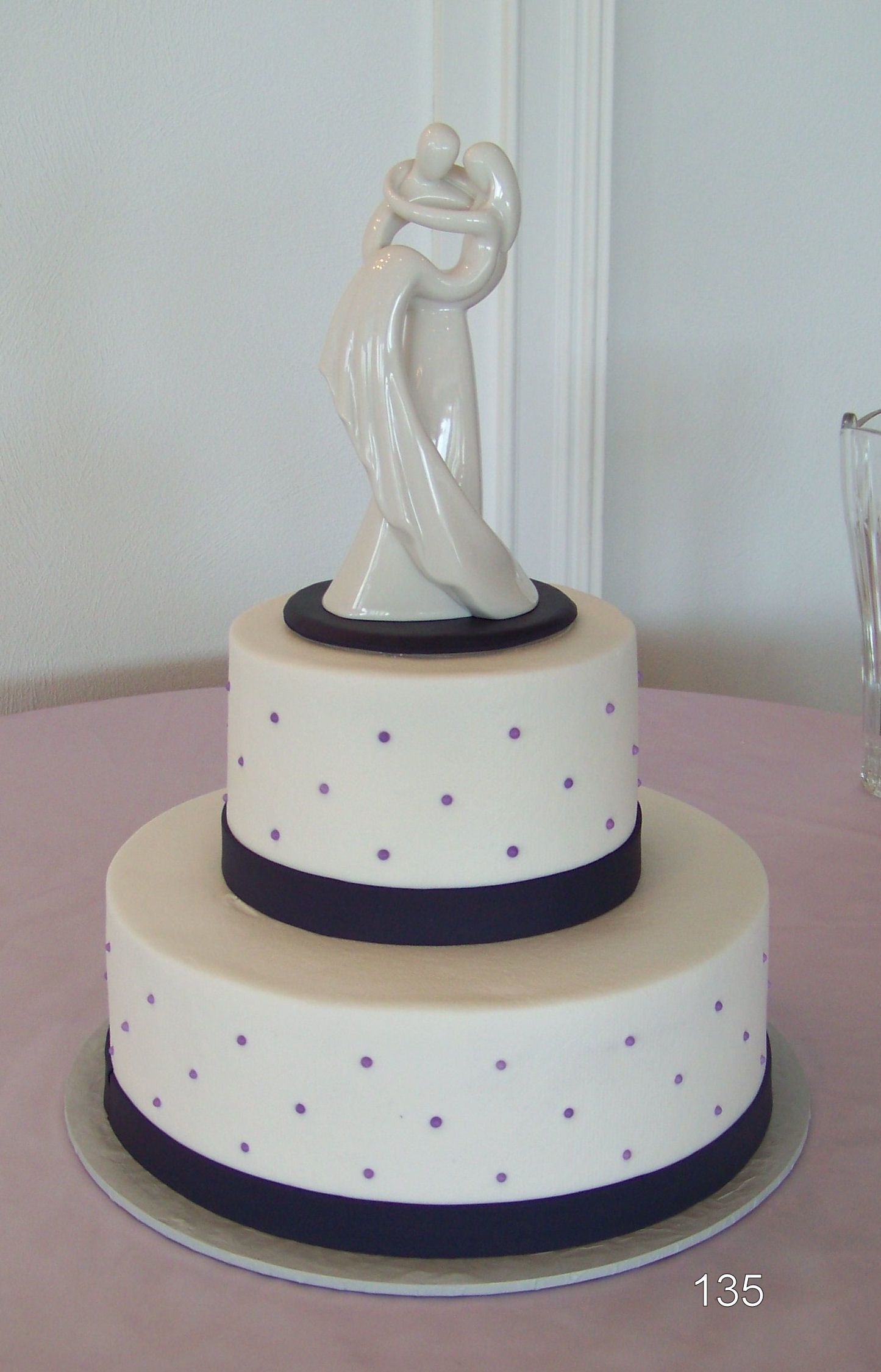Two-tier white wedding cake with dark ribbon accents and a white bride-and-groom topper