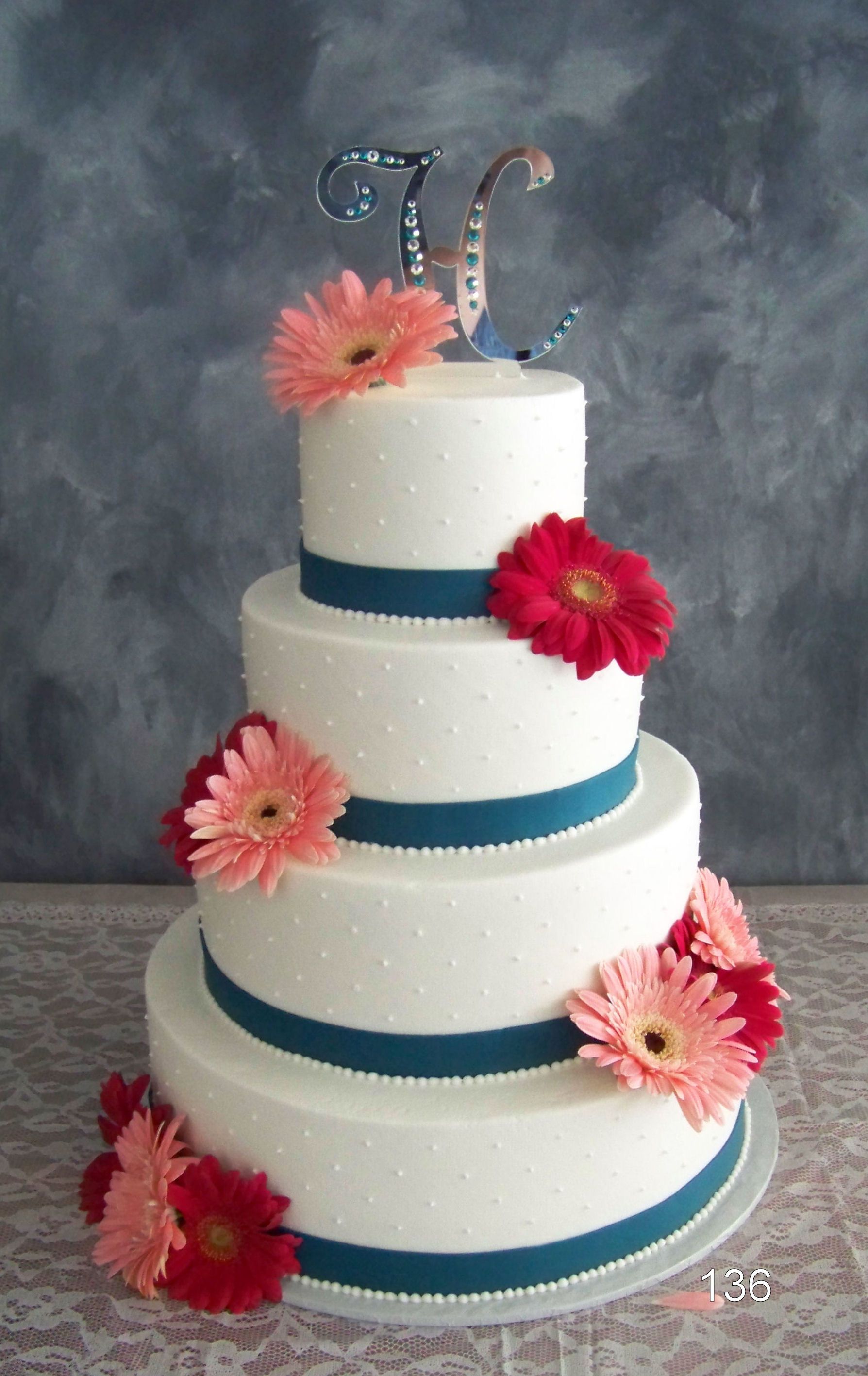 Four-tier white cake with blue ribbon bands and pink flowers, topped with silver glitter “50” candles