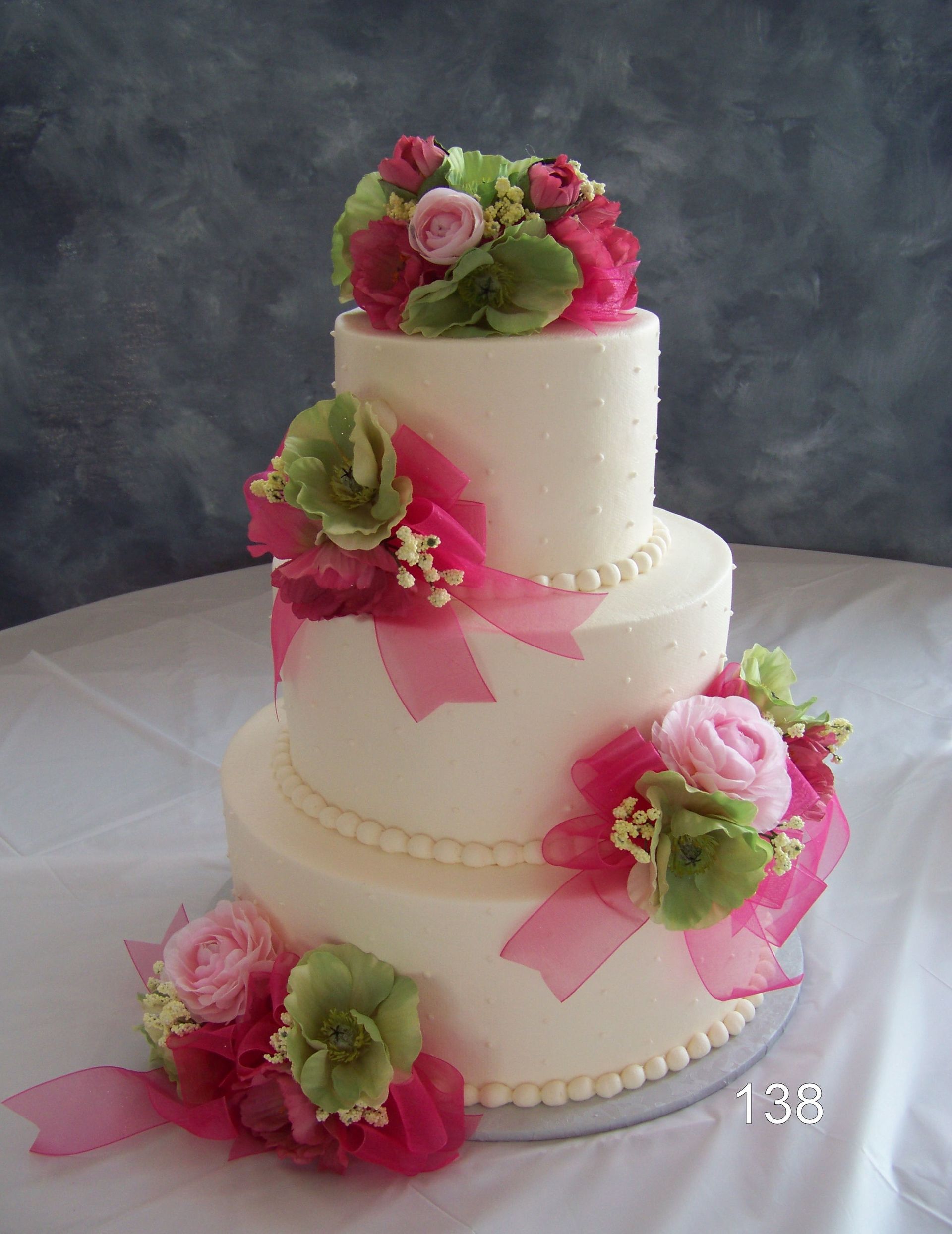 Three-tier white wedding cake with pink and green floral decorations on a table