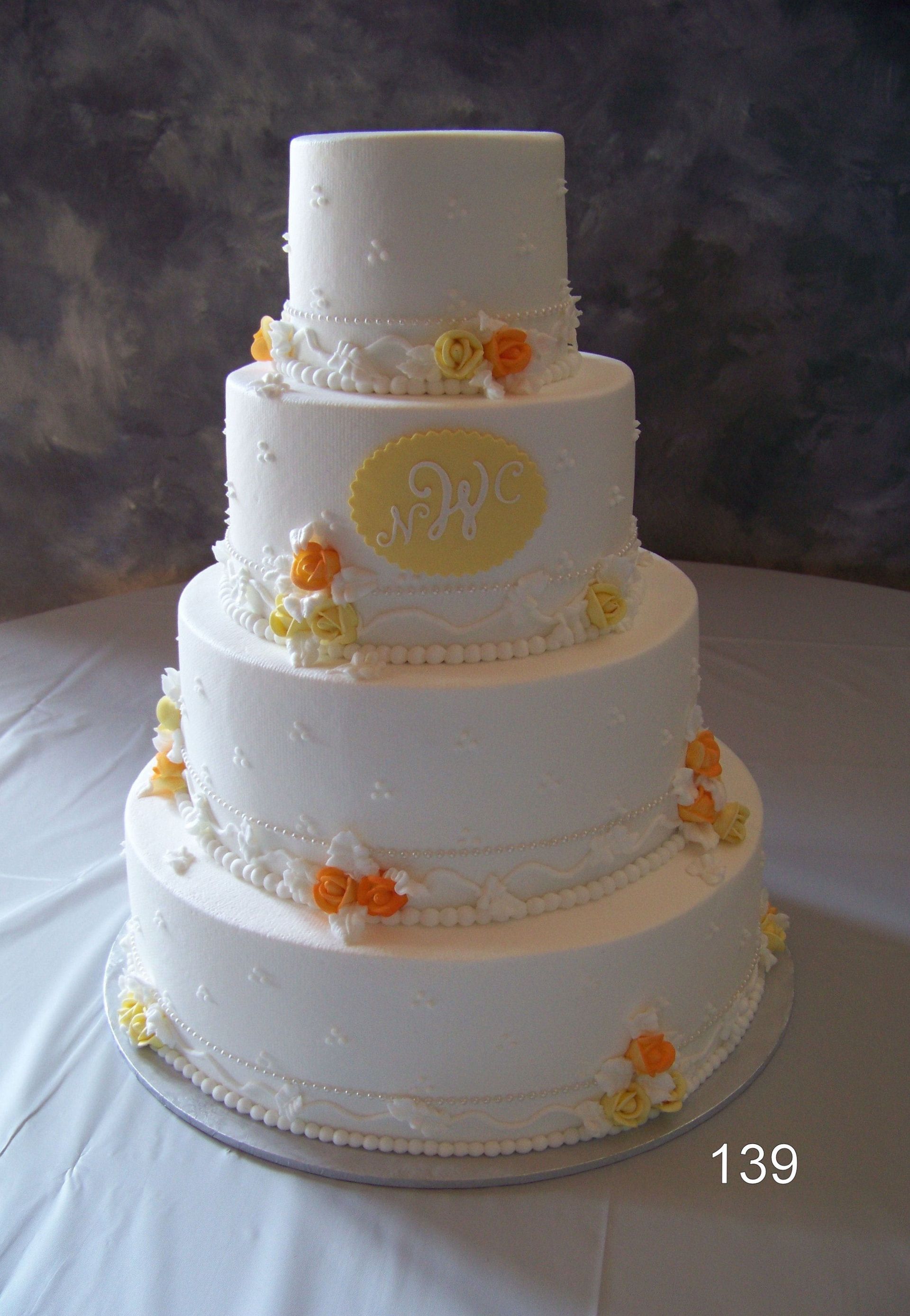 Four-tier white wedding cake with yellow and orange floral accents on a stand