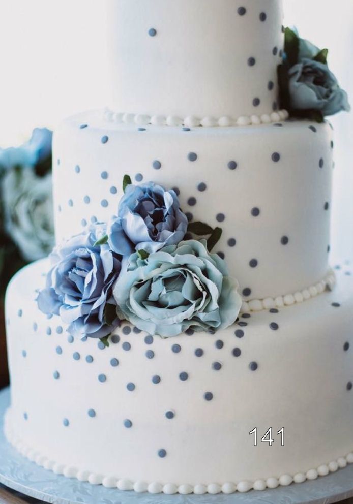 White tiered cake with silver polka dots and blue flowers on the lower tier