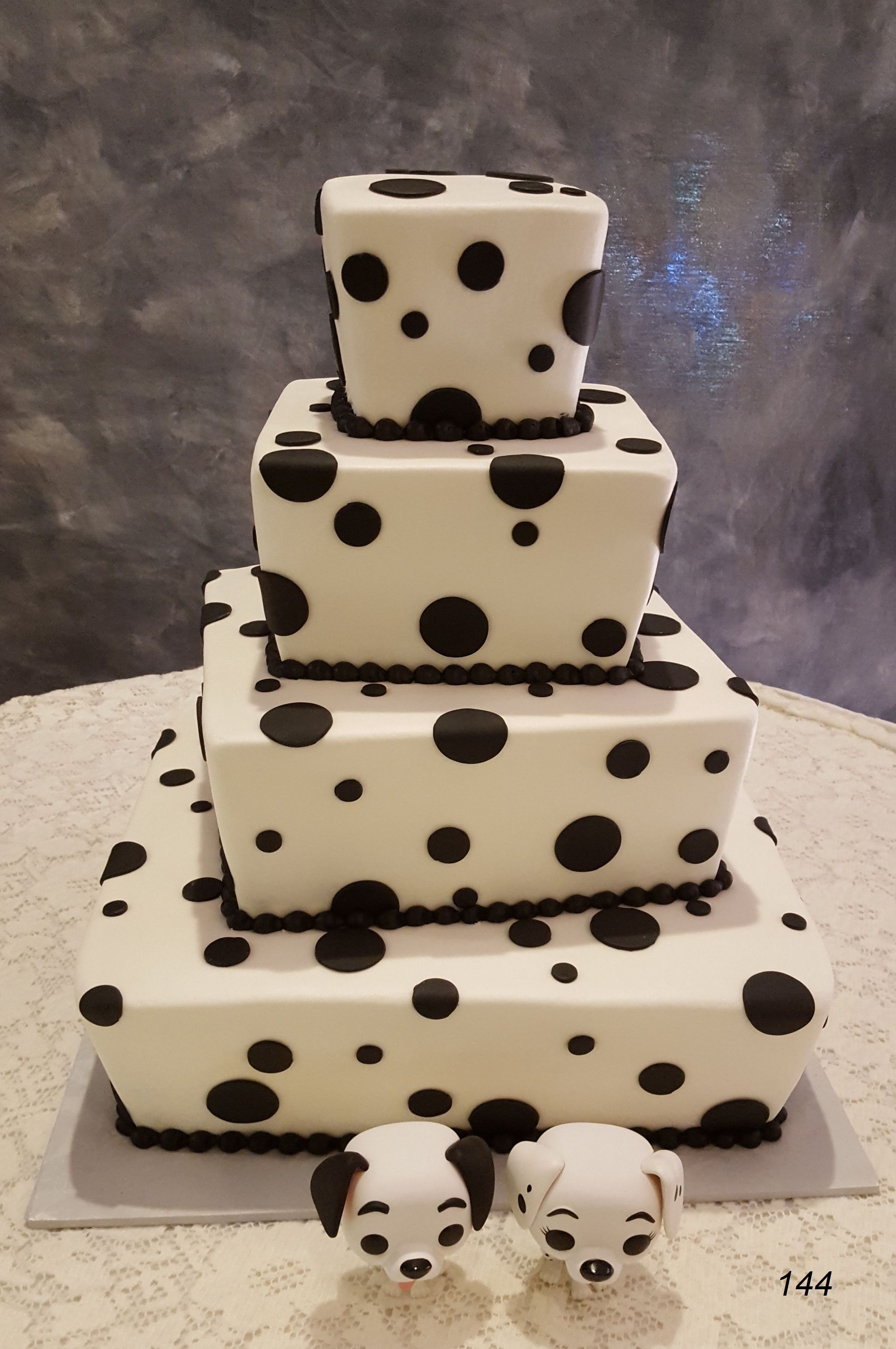 Stacked white cake with black polka dots and two matching puppy cake toppers on a white cake board