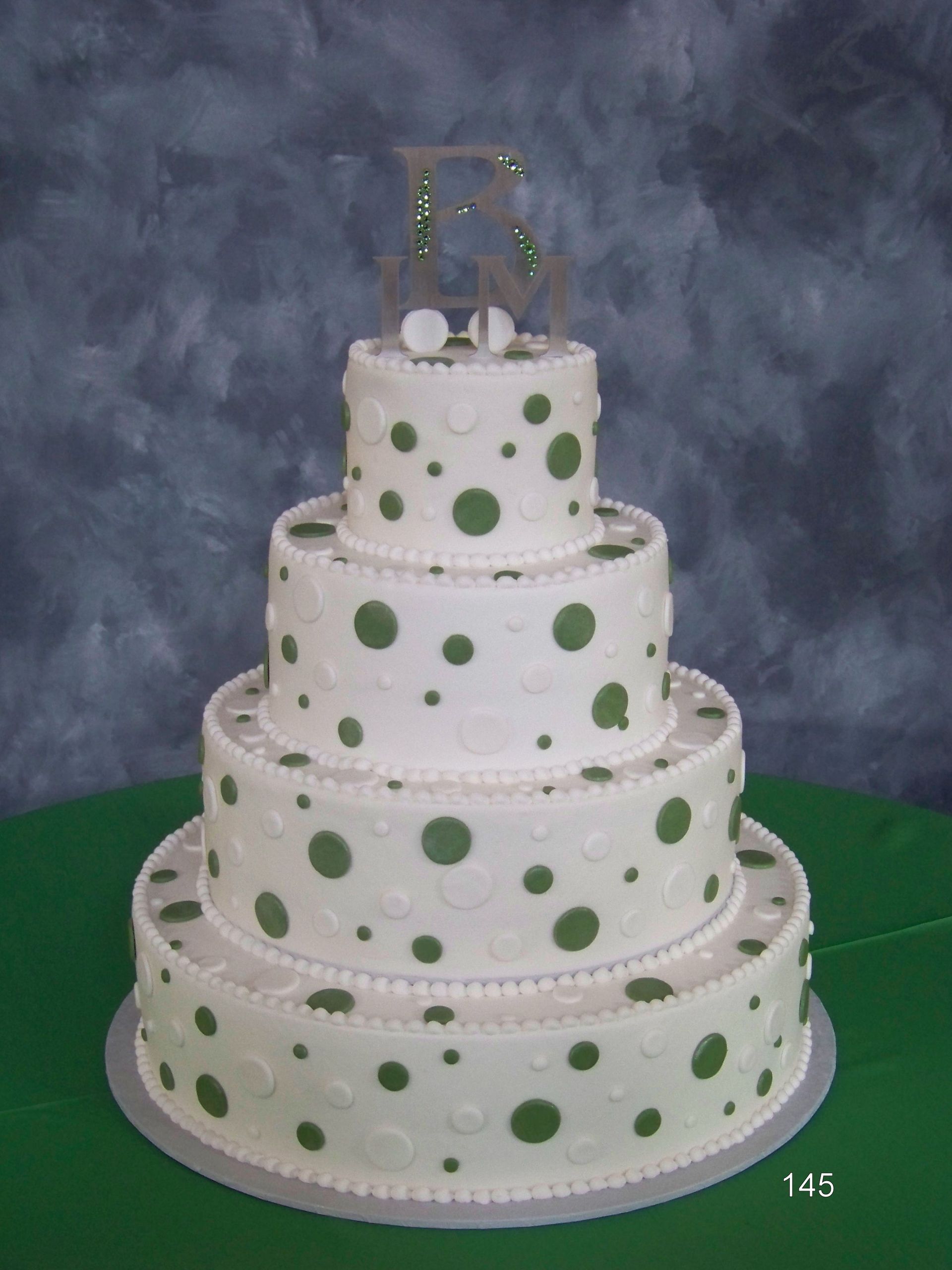 White tiered cake with green polka dots and silver trim on a green tablecloth