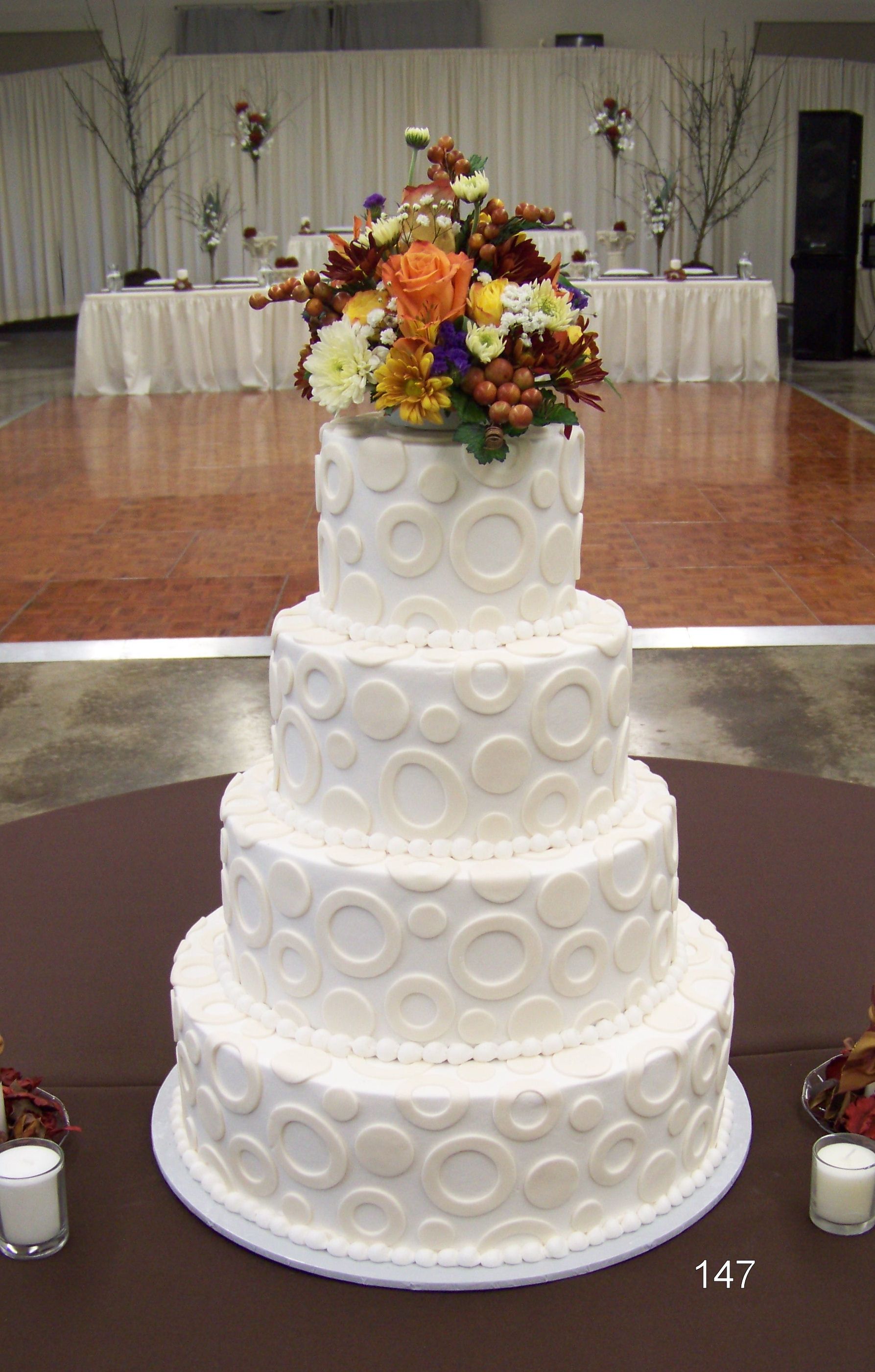 White four-tier wedding cake with floral topper on a table in a banquet hall