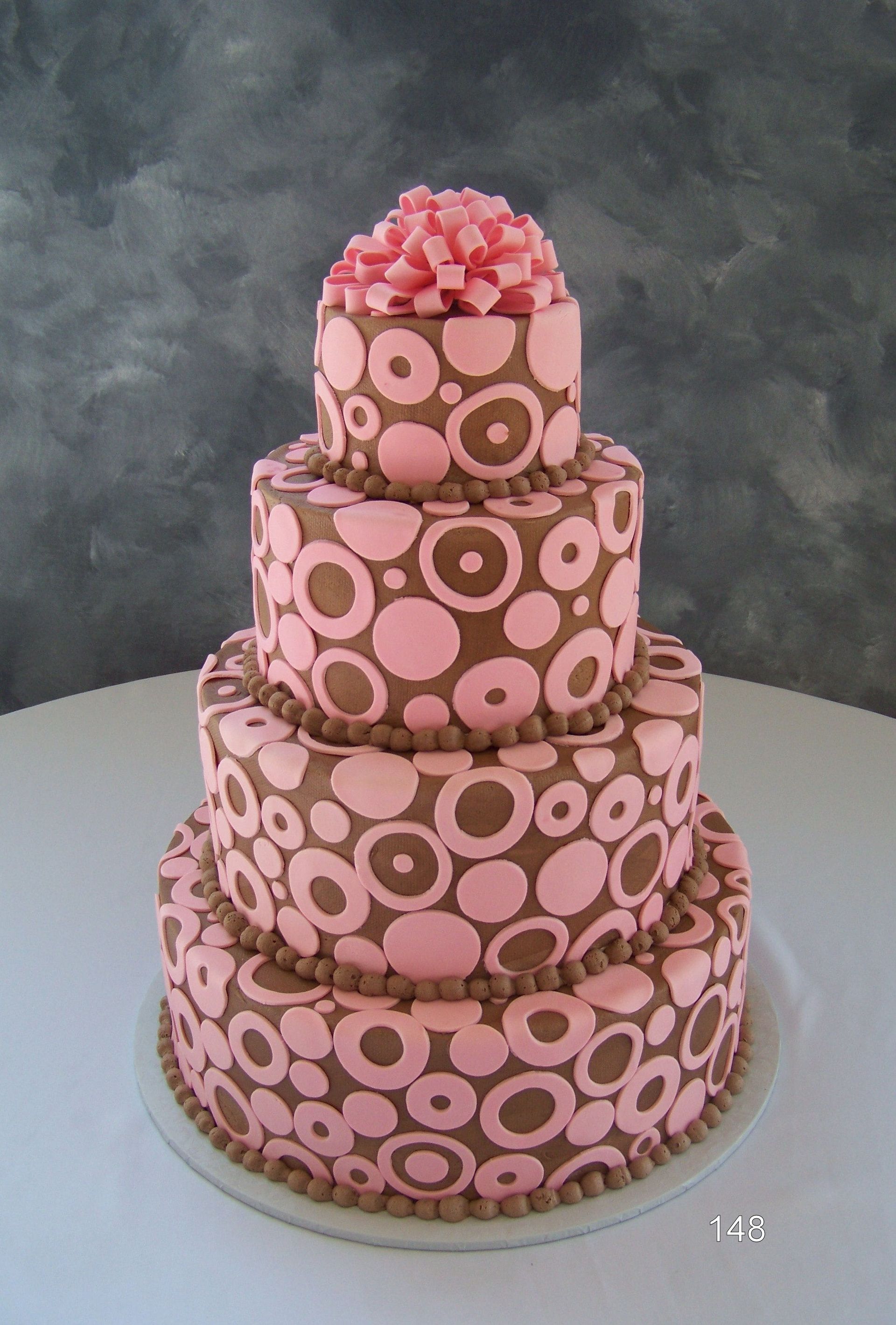 Pink tiered cake with circular pattern and bow on top, displayed on a white stand
