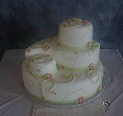 Three-tier white cake with green swirls and pink flowers on a table against a dark backdrop