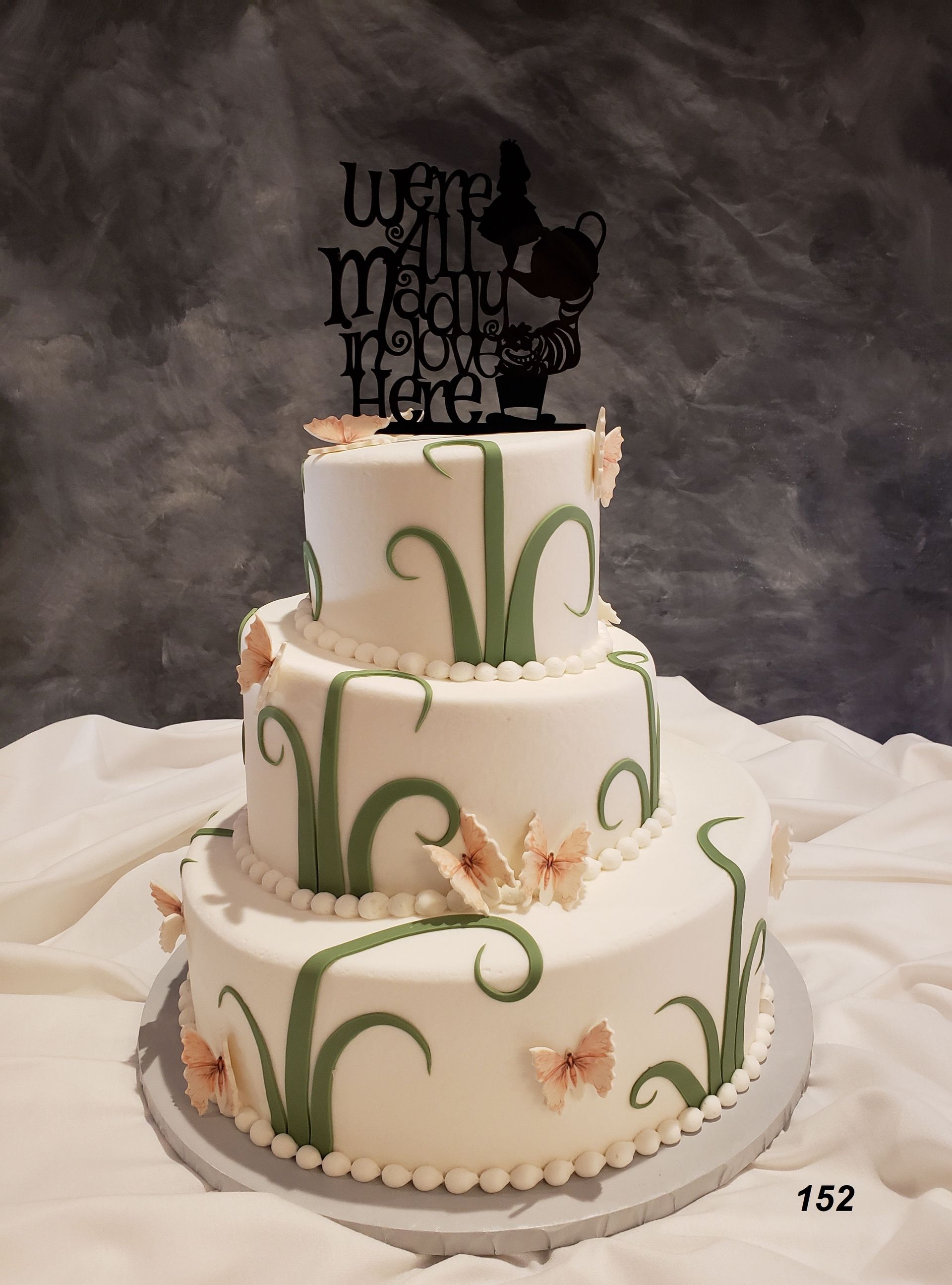 Three-tier white wedding cake with green vine decorations and black topper on a table