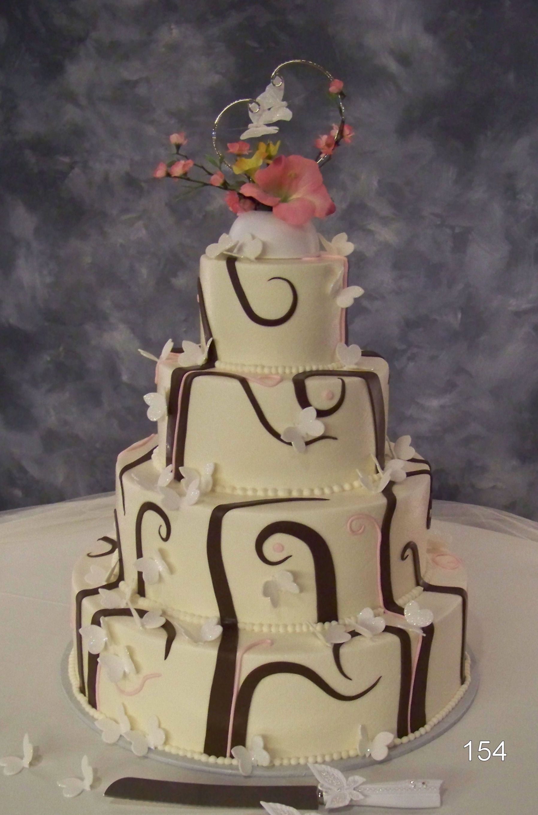 Three-tier white and brown decorated cake with pink flowers on top against a gray backdrop
