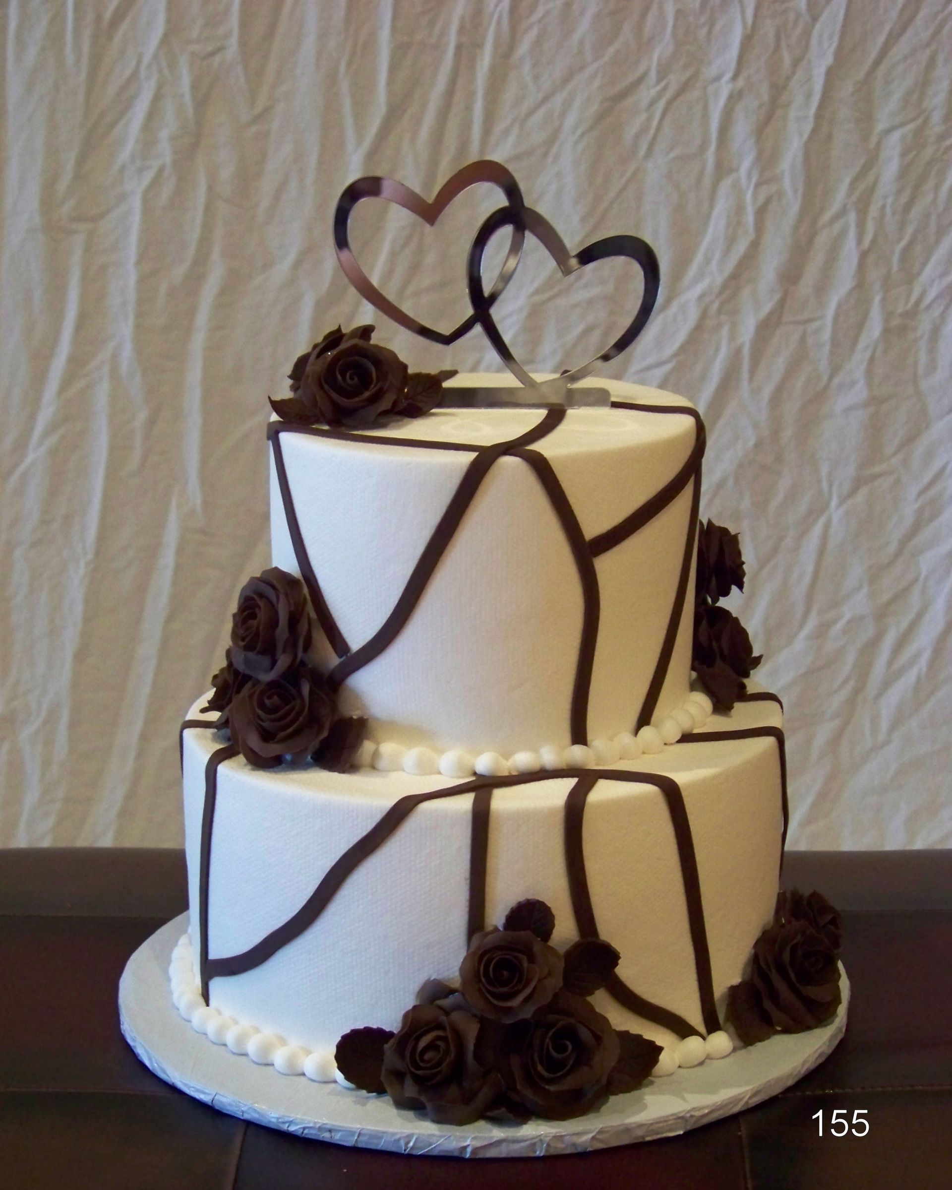 White two-tier wedding cake with chocolate drips, roses, and heart toppers