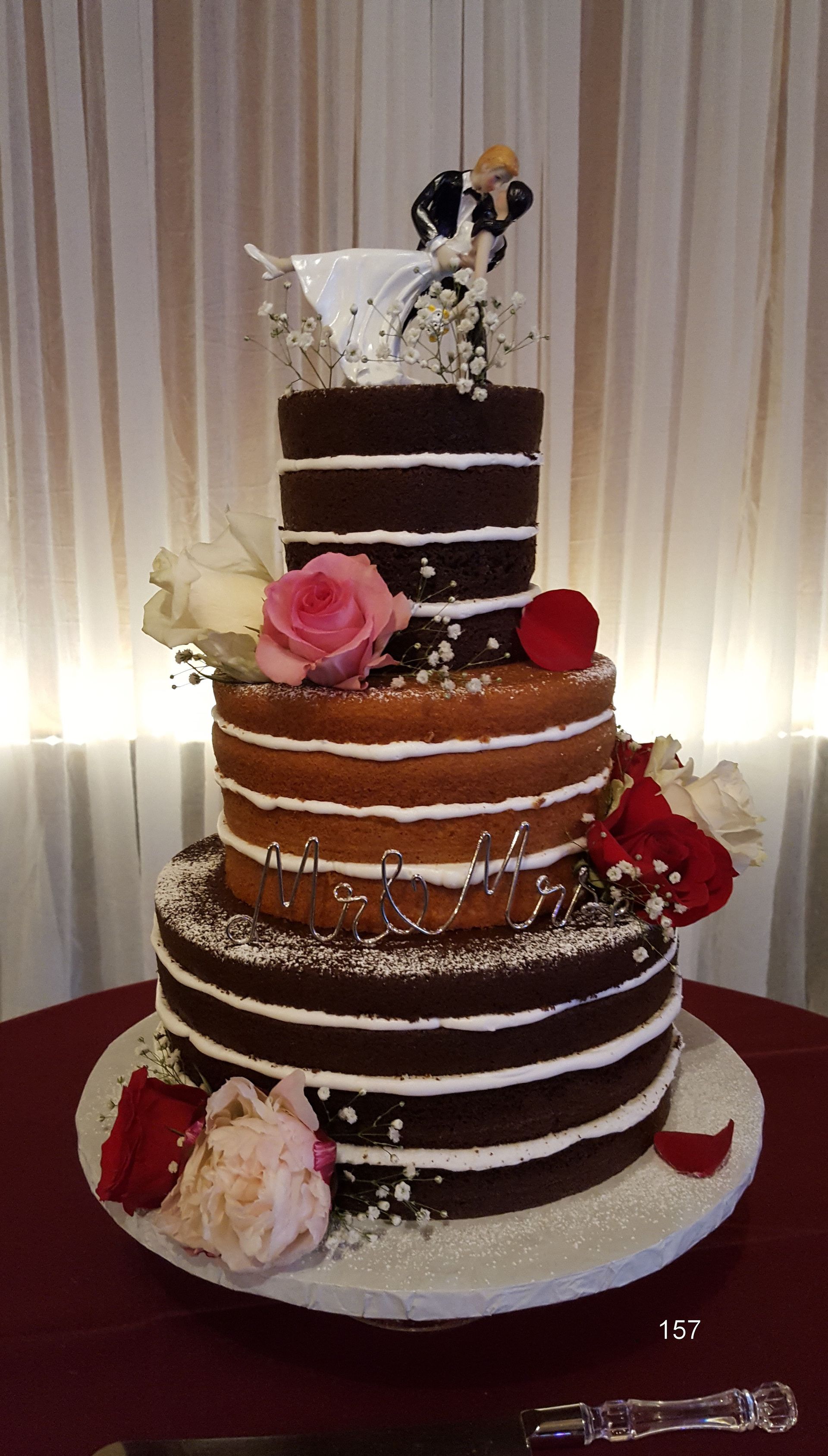 Three-tiered chocolate and white wedding cake with flowers on a table, topped with a bride and groom figurine