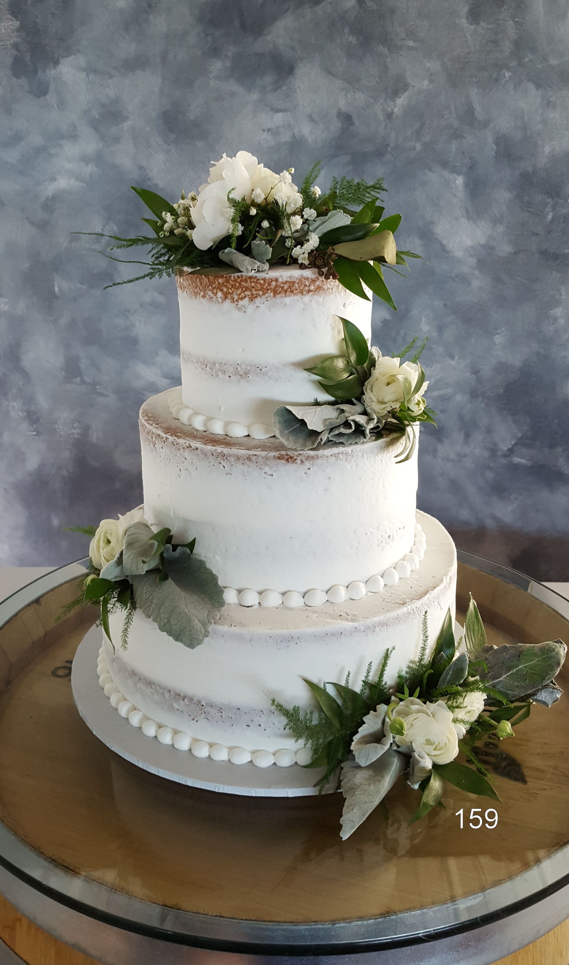 Three-tier white wedding cake with greenery and white flowers on a wooden board