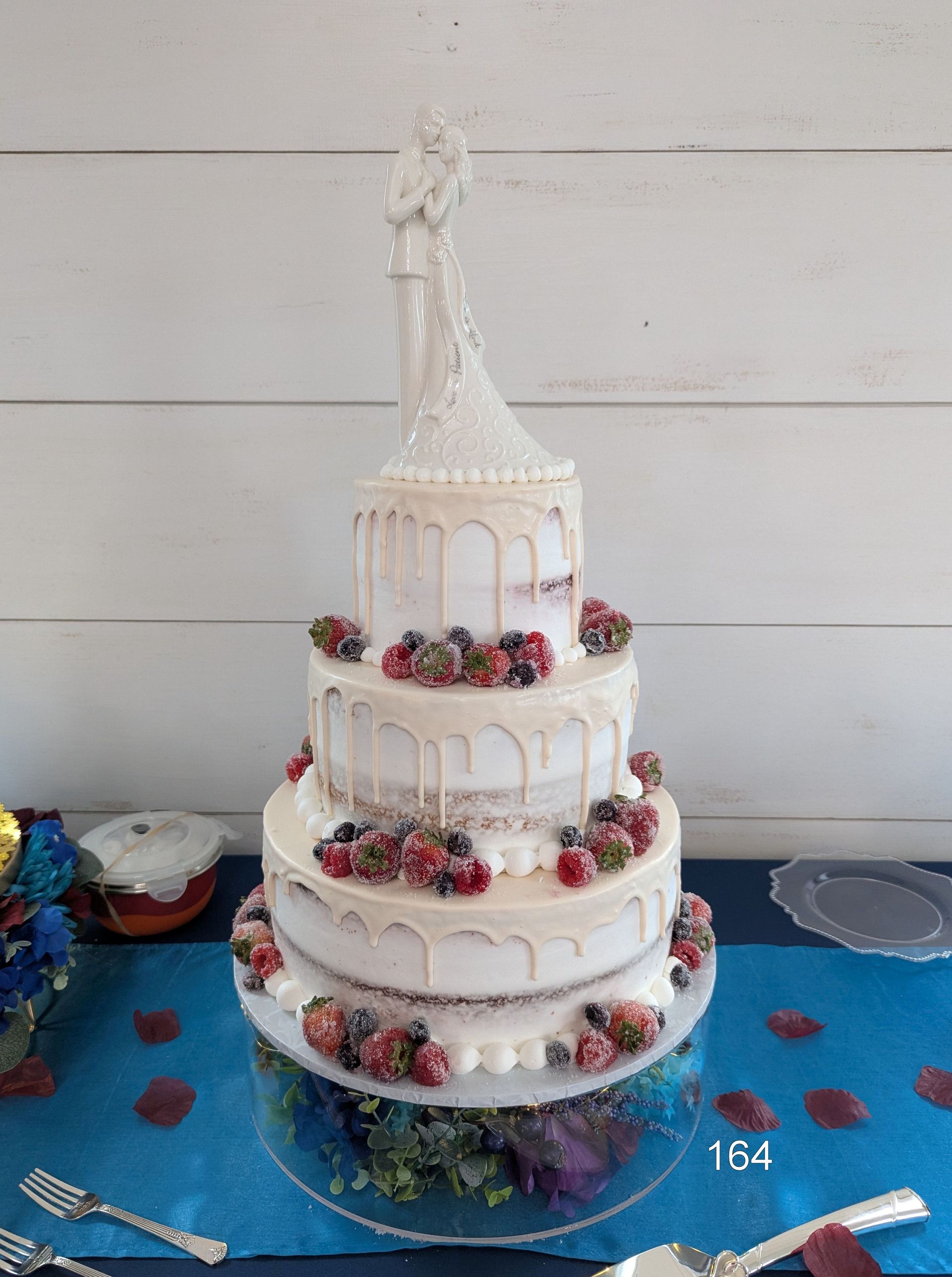 Tall white tiered cake with floral decorations and a bride topper on a blue table