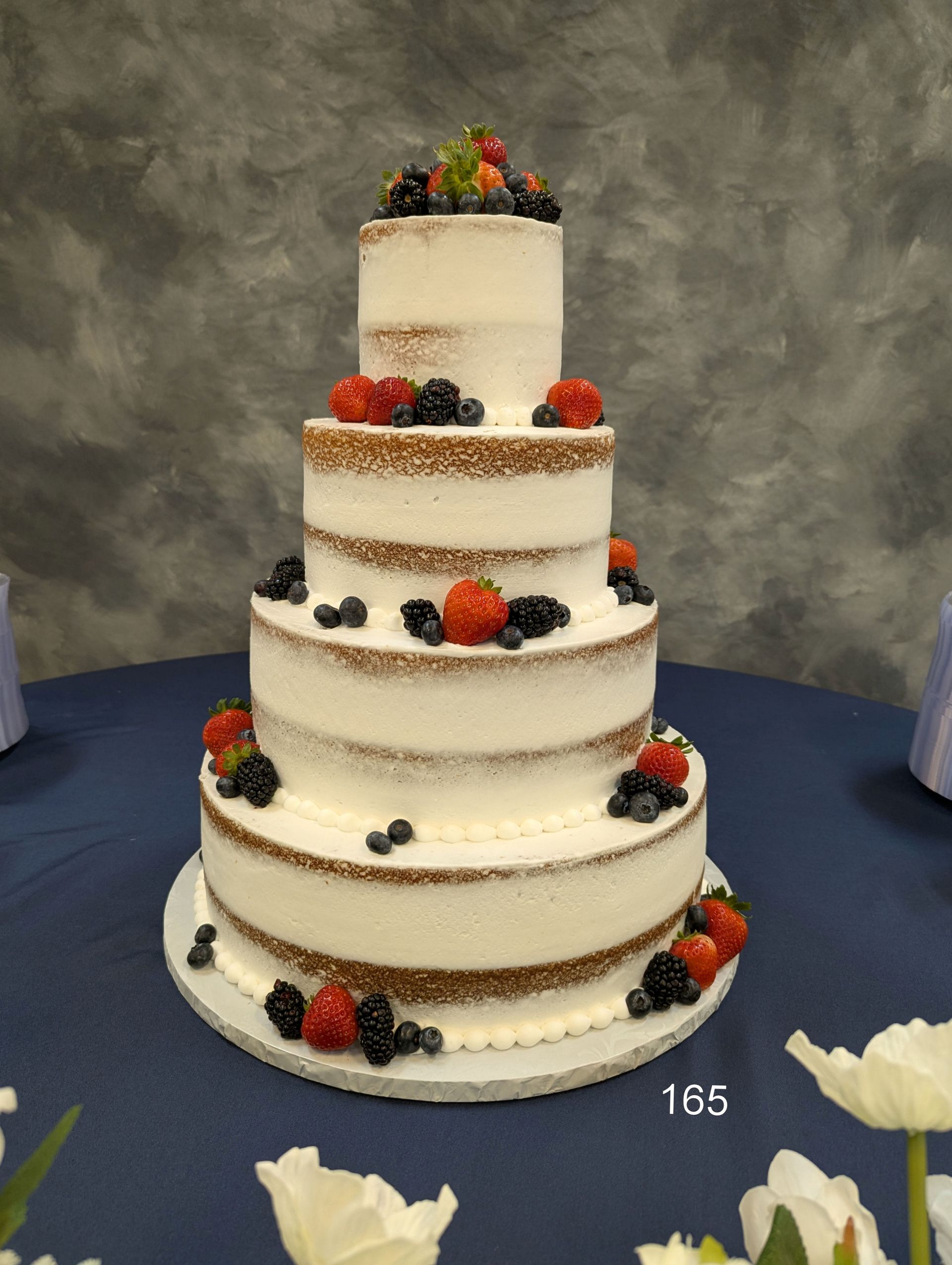 Five-tier white wedding cake with berries and flowers on a blue tablecloth