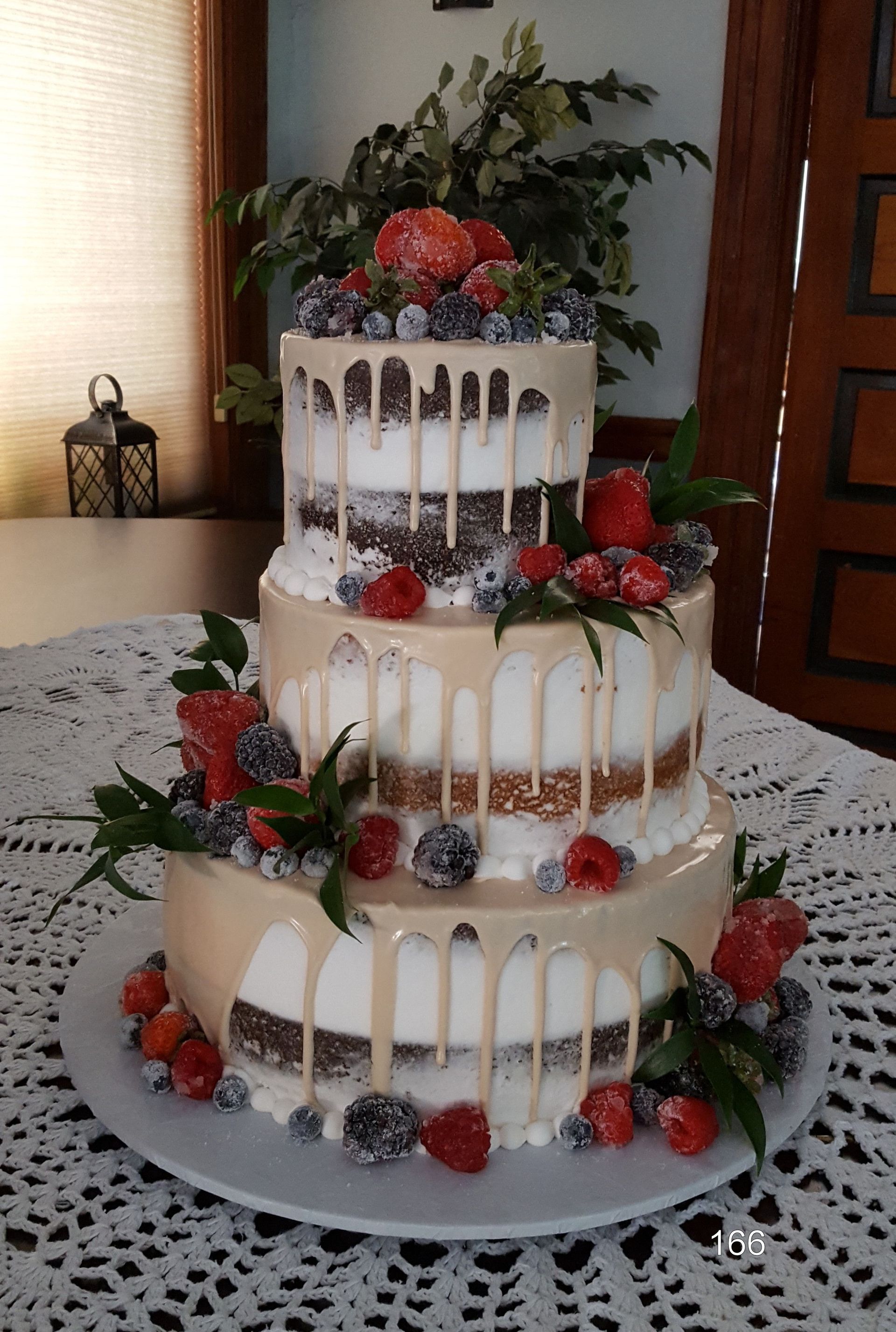 Three-tier white wedding cake with berries and greenery on a table