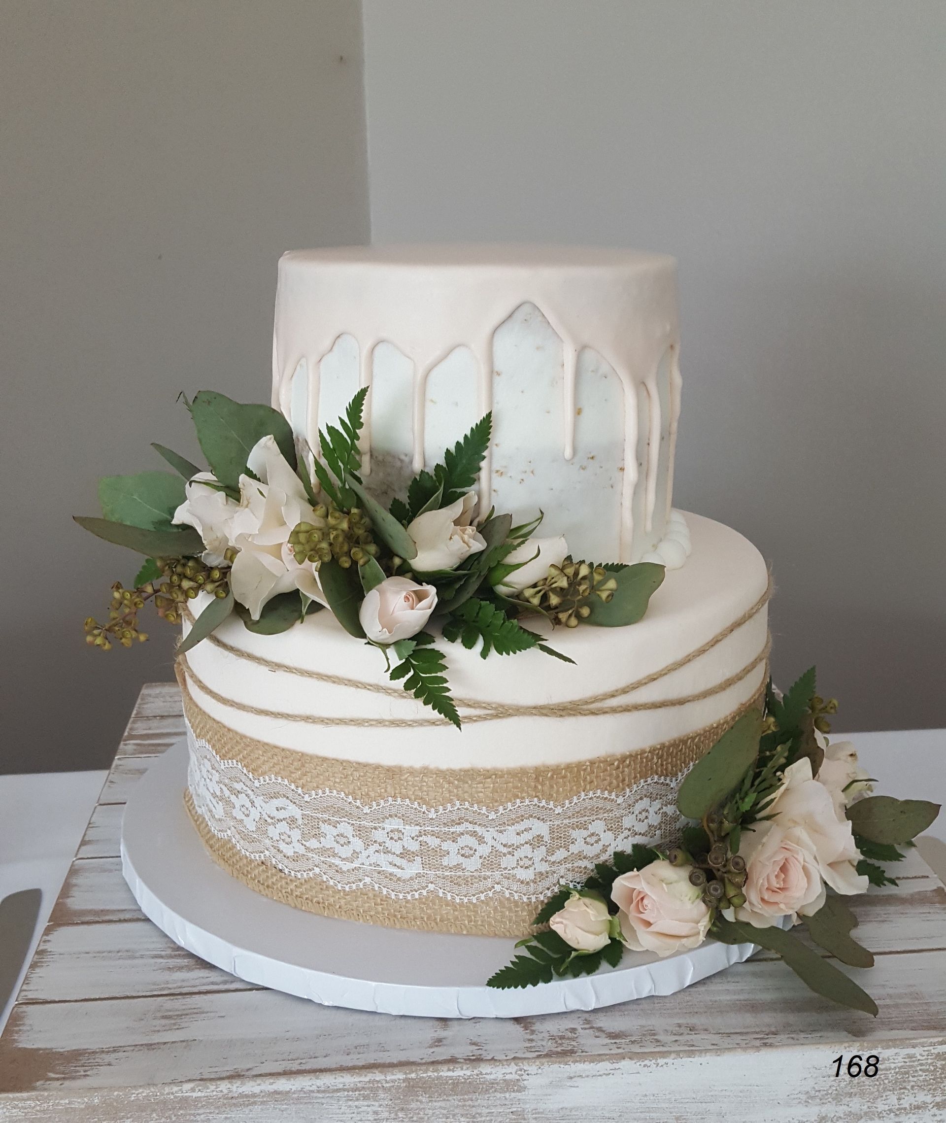 Two-tier white cake with gold accents and white floral decorations on a rustic board