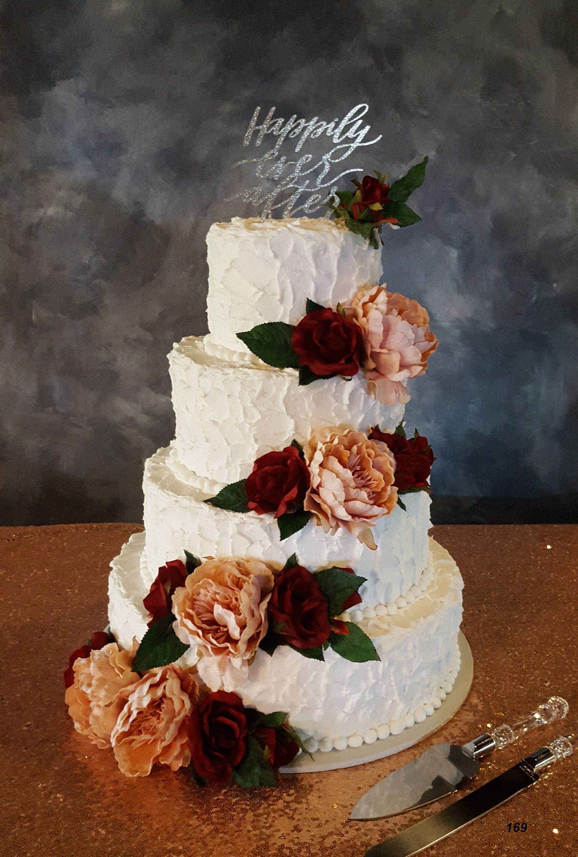 Three-tier white wedding cake with peach and burgundy flowers and a topper on a wooden table