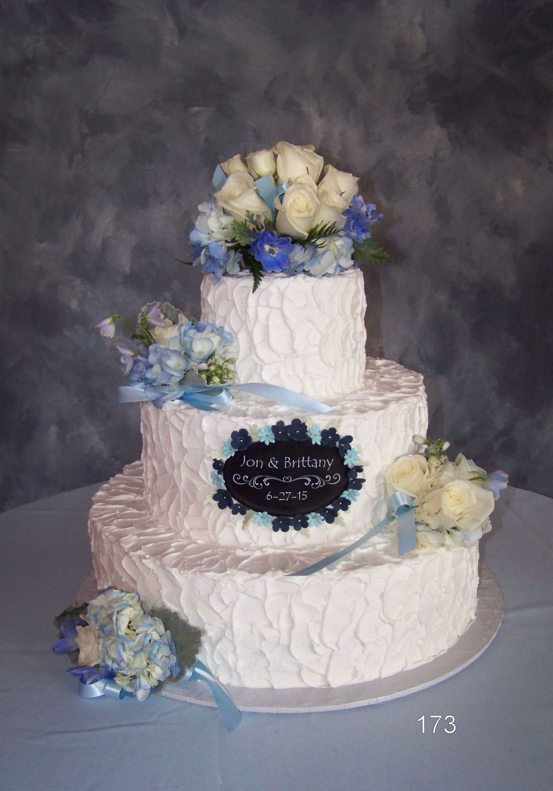 Three-tier white cake with blue and white flowers on a gray backdrop