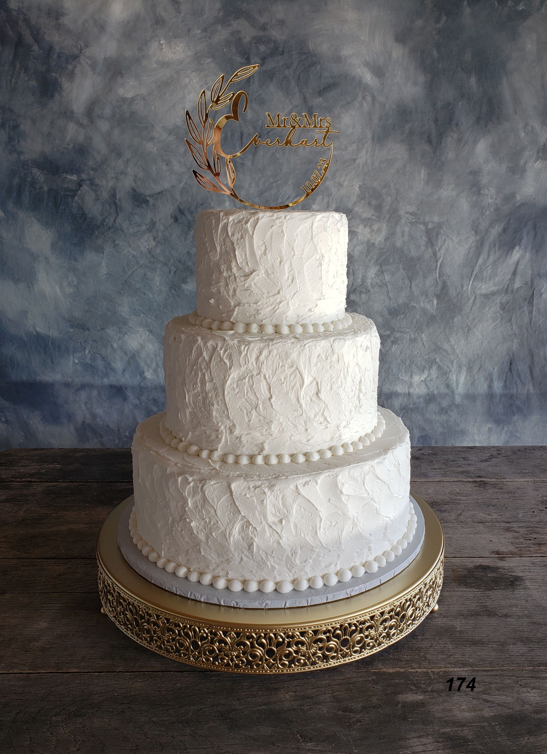 Three-tier white wedding cake with gold swan topper and ornate gold base on a rustic table
