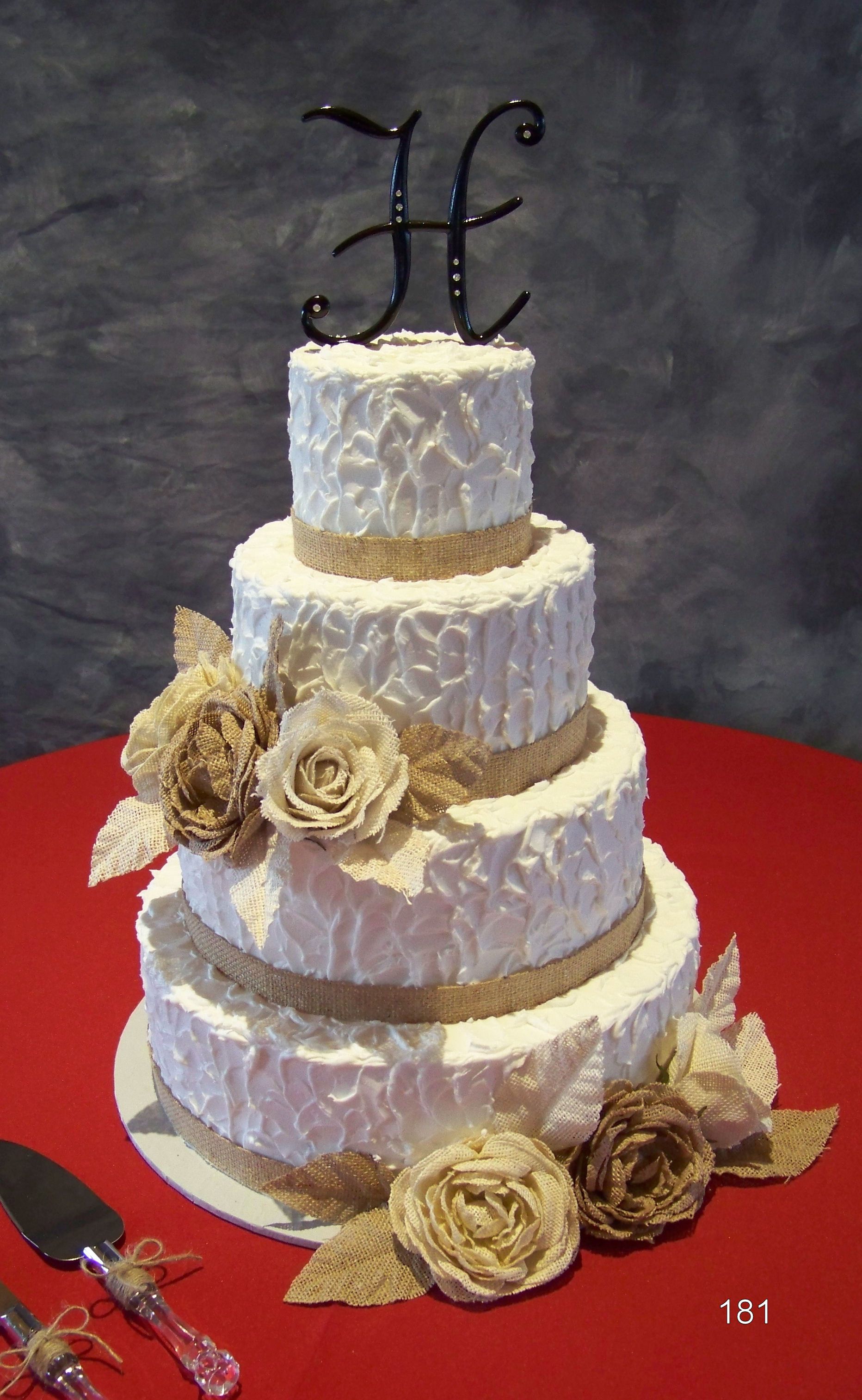 Three-tier white and lavender cake with gold flowers and black monogram topper on a red table