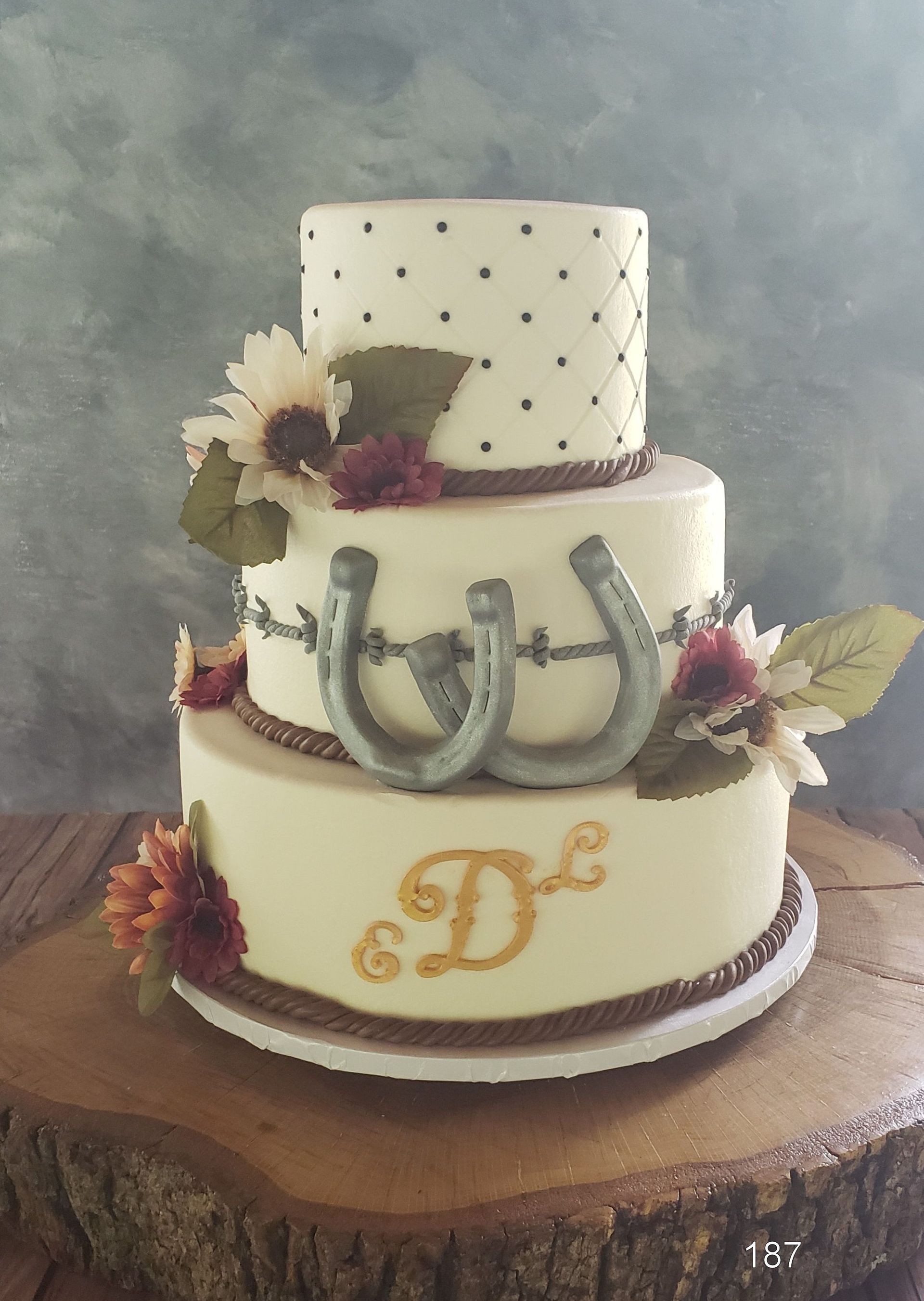 Three-tier white cake with silver stethoscope decor, flowers, and gold monogram on a wood slab